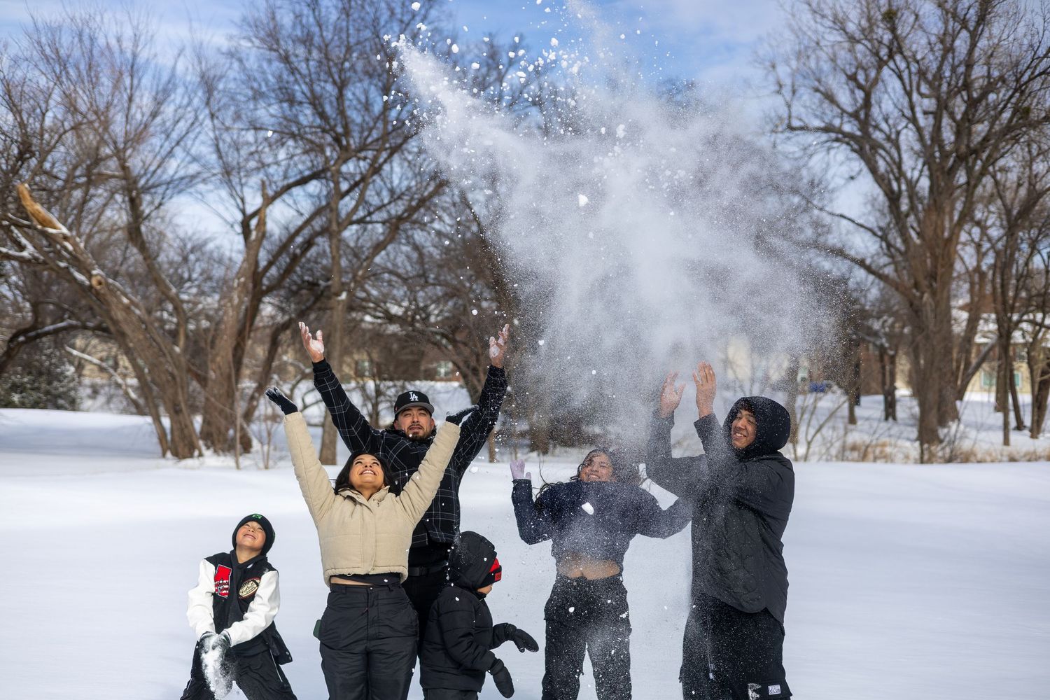 People enjoying a winter day by throwing snow in the air at a snow-covered park.
