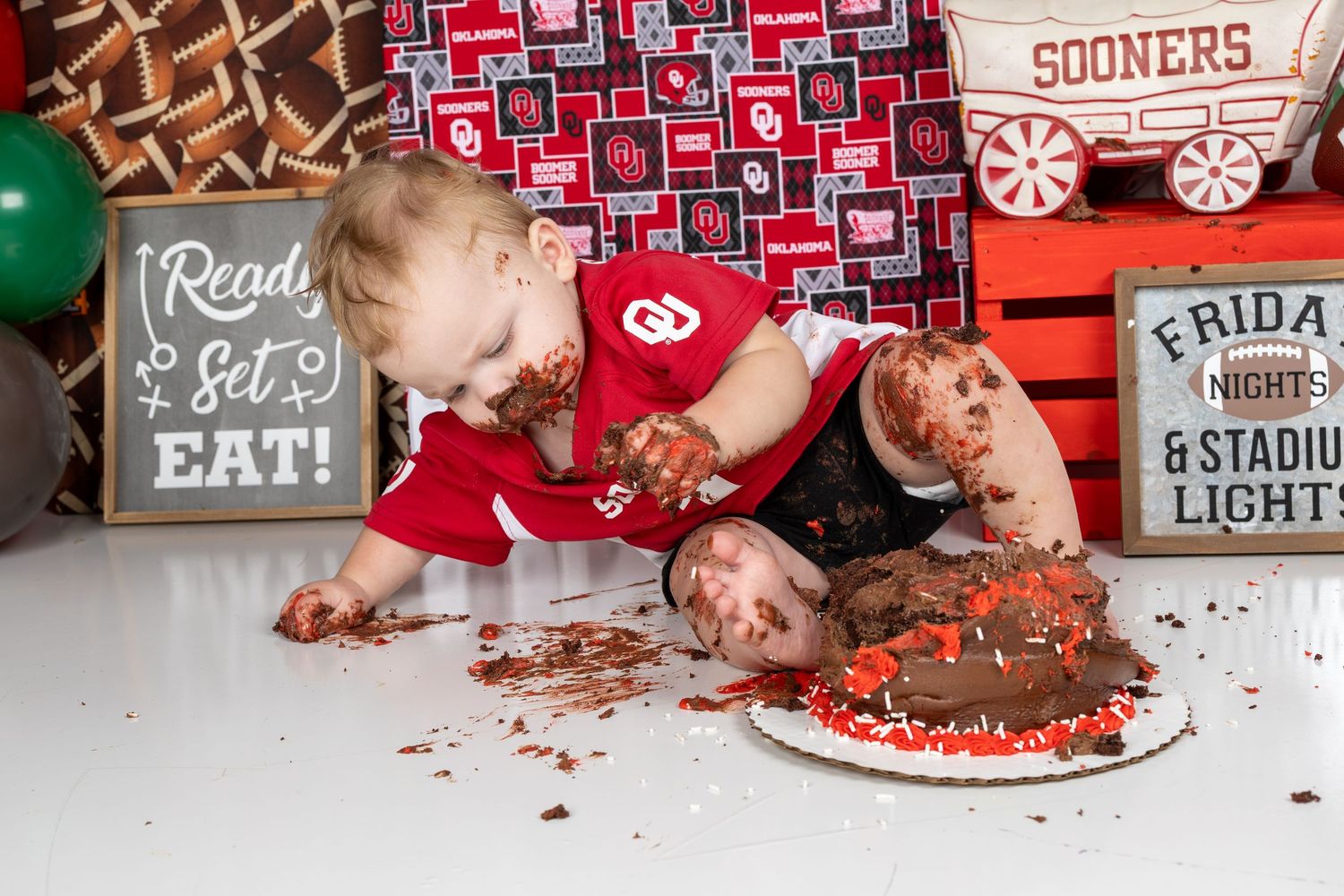Baby smashing chocolate cake at Oklahoma Sooners themed first birthday cake smash photo session.