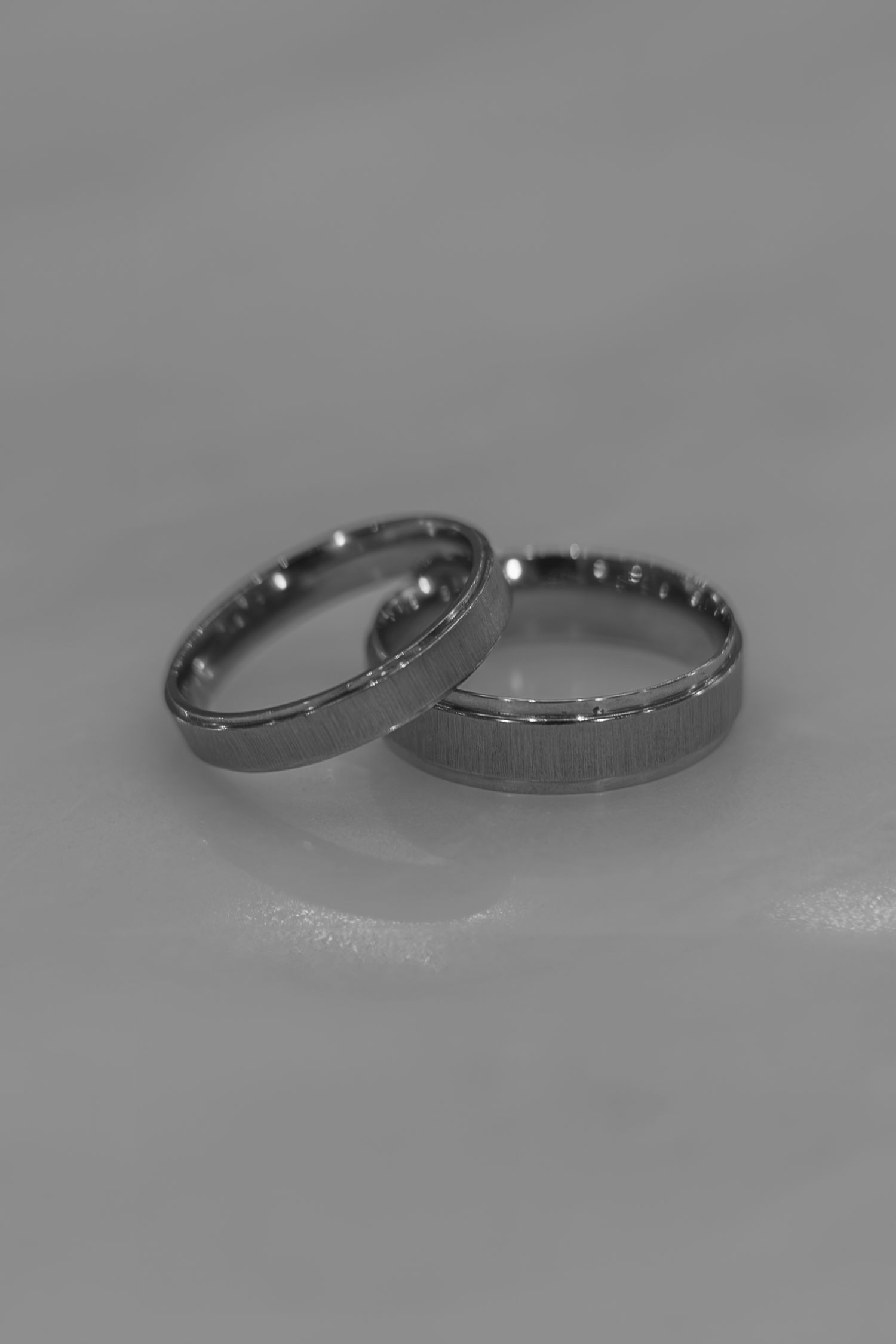 Two silver tungsten carbide wedding bands with brushed finish and beveled edges displayed on gray surface.