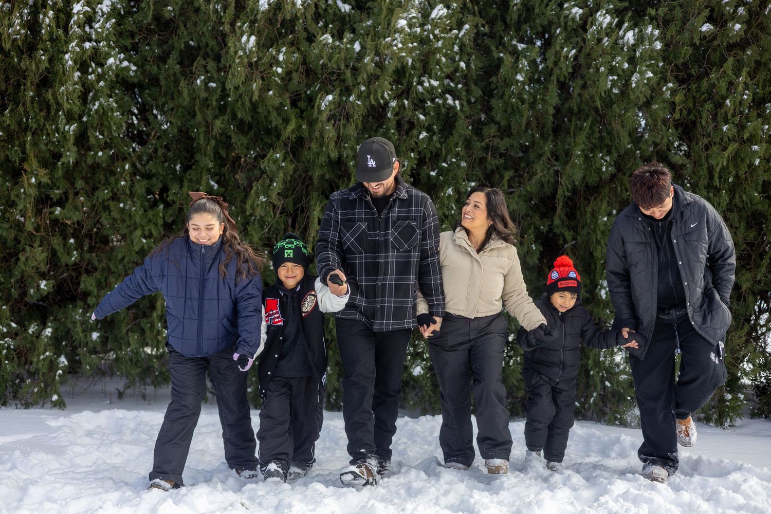 A sequence of winter snow action shots showing people walking and playing in deep snow against an evergreen backdrop.