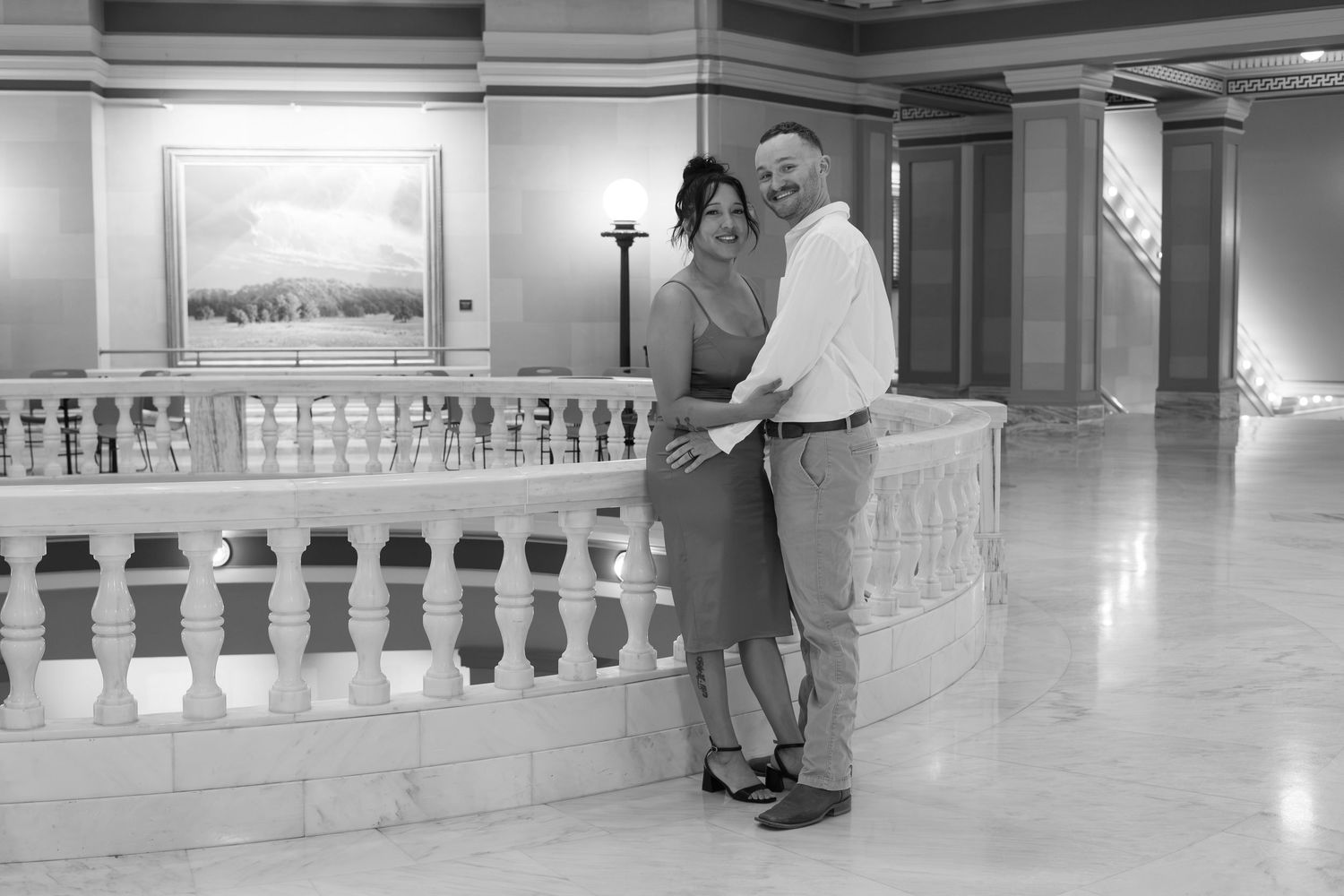 Black and white photo of a couple embracing and smiling in an elegant marble ballroom interior.
