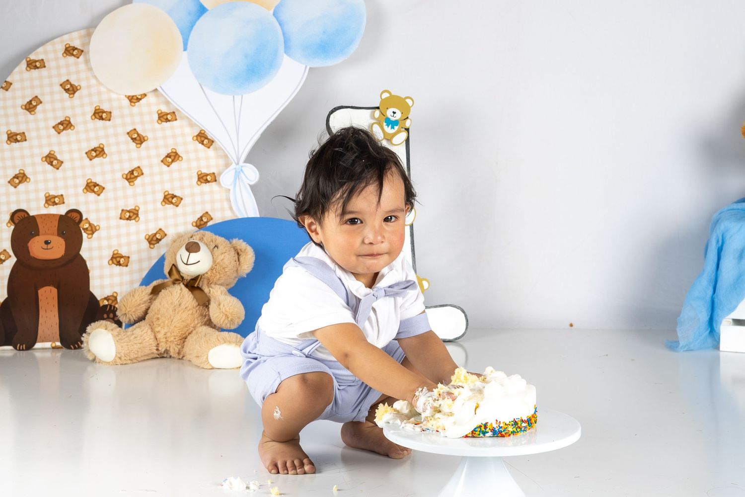 Baby boy celebrates first birthday with smash cake, teddy bears, and blue balloons in a festive photo session.