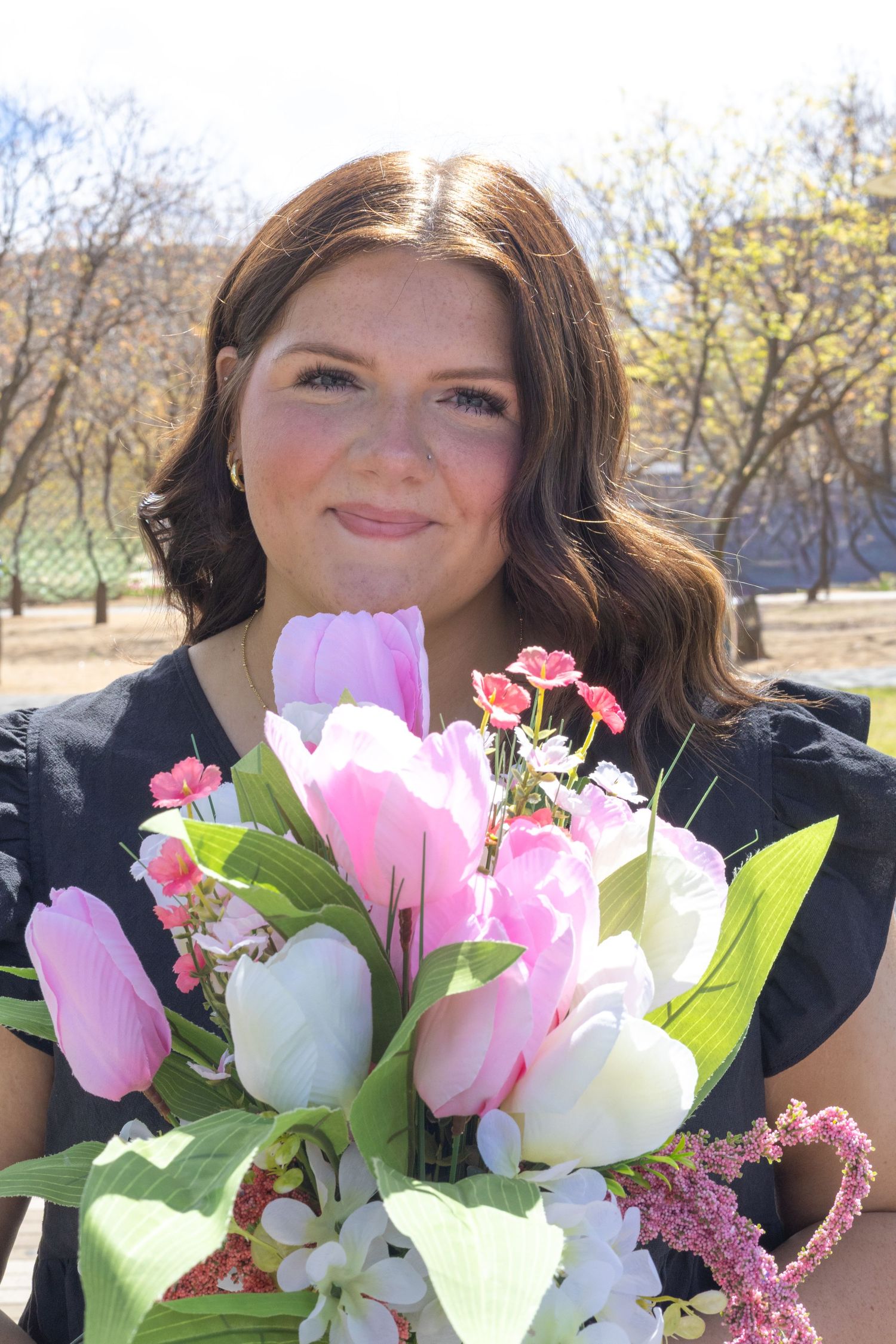 A bouquet of pink tulips and white flowers is held against a natural outdoor background.