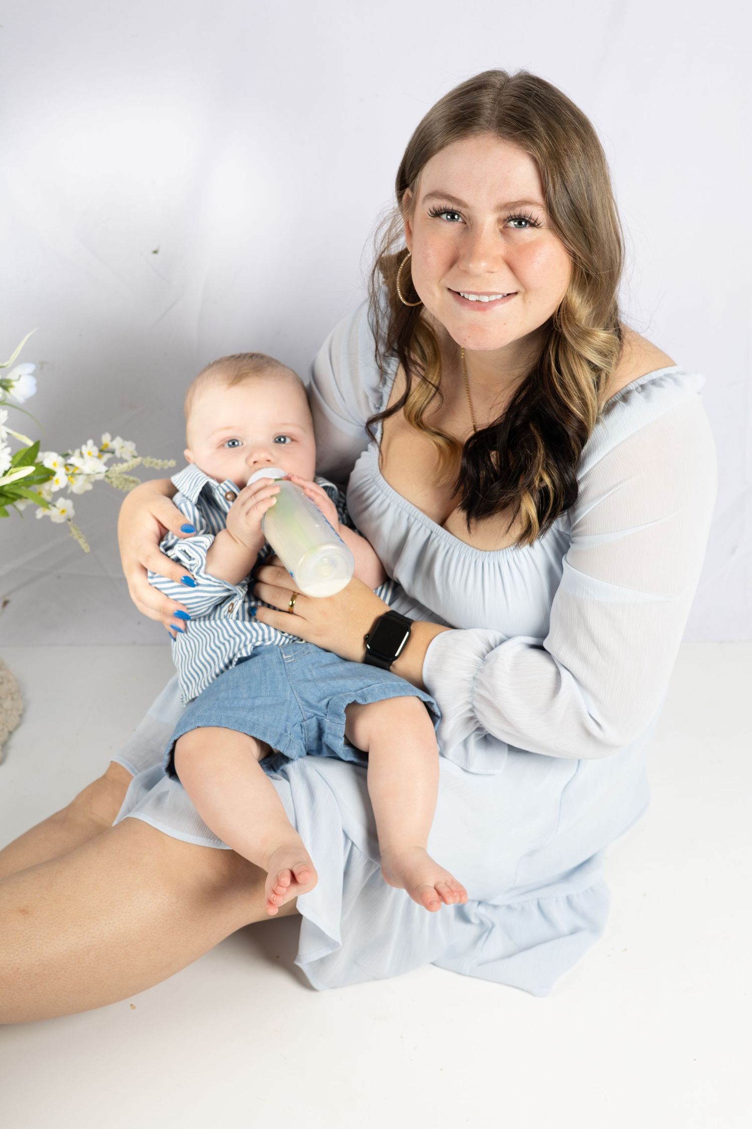 Mother and baby in matching blue and white outfits pose together on white backdrop during professional photoshoot.