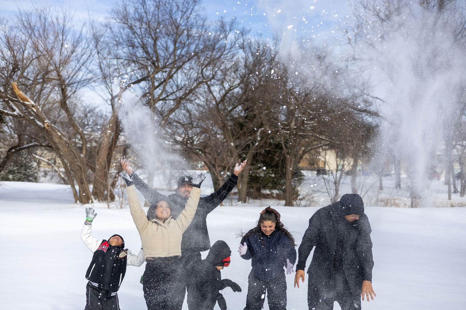 A group of people playing in the snow during winter, throwing snowballs and enjoying outdoor winter activities.
