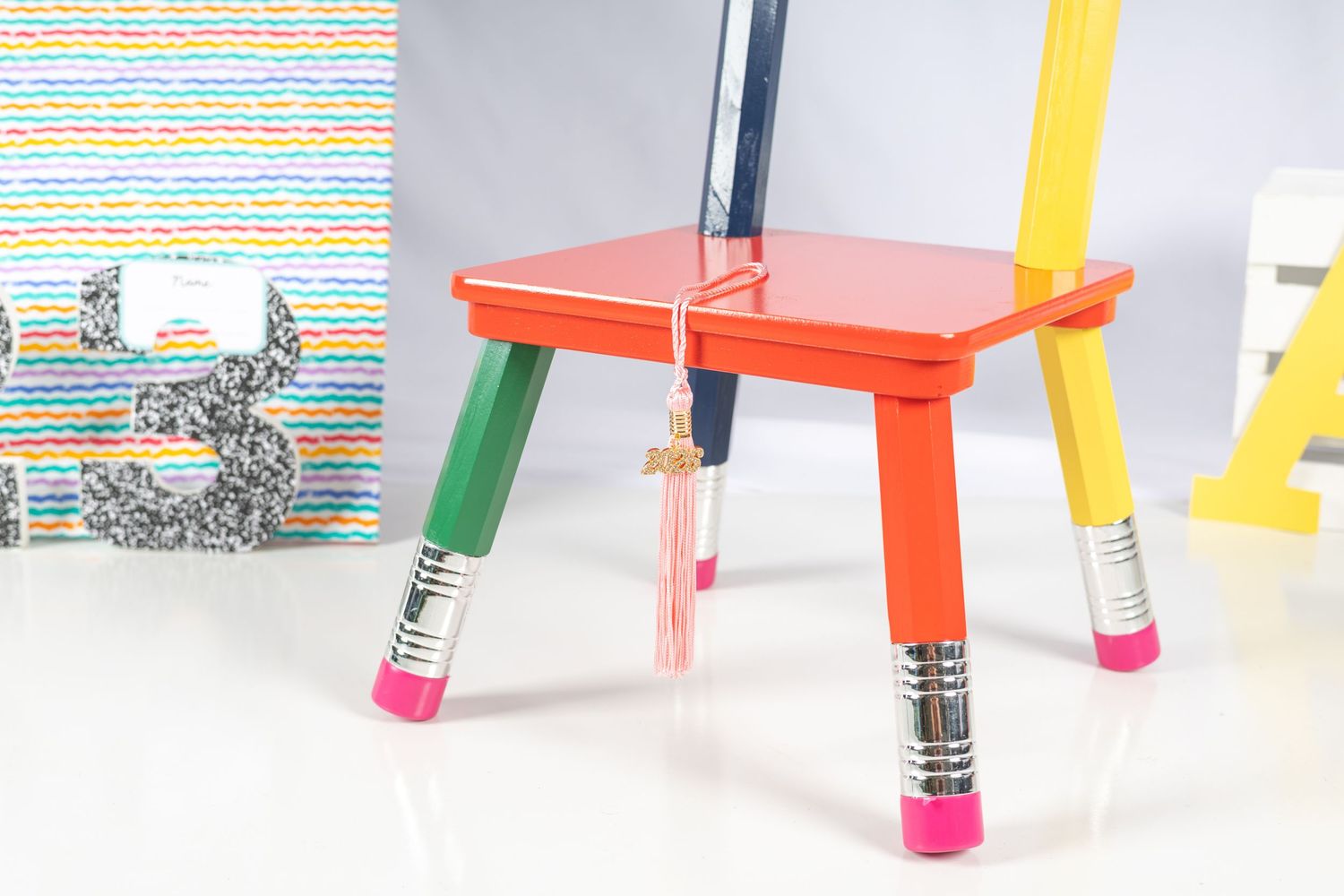 Colorful children's stool with pencil-shaped legs in red, green, yellow, and pink on a white background.