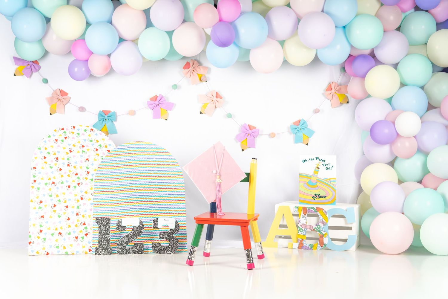 Colorful pastel balloon garland backdrop with children's chairs, gifts, and ice cream decorations for a birthday party.