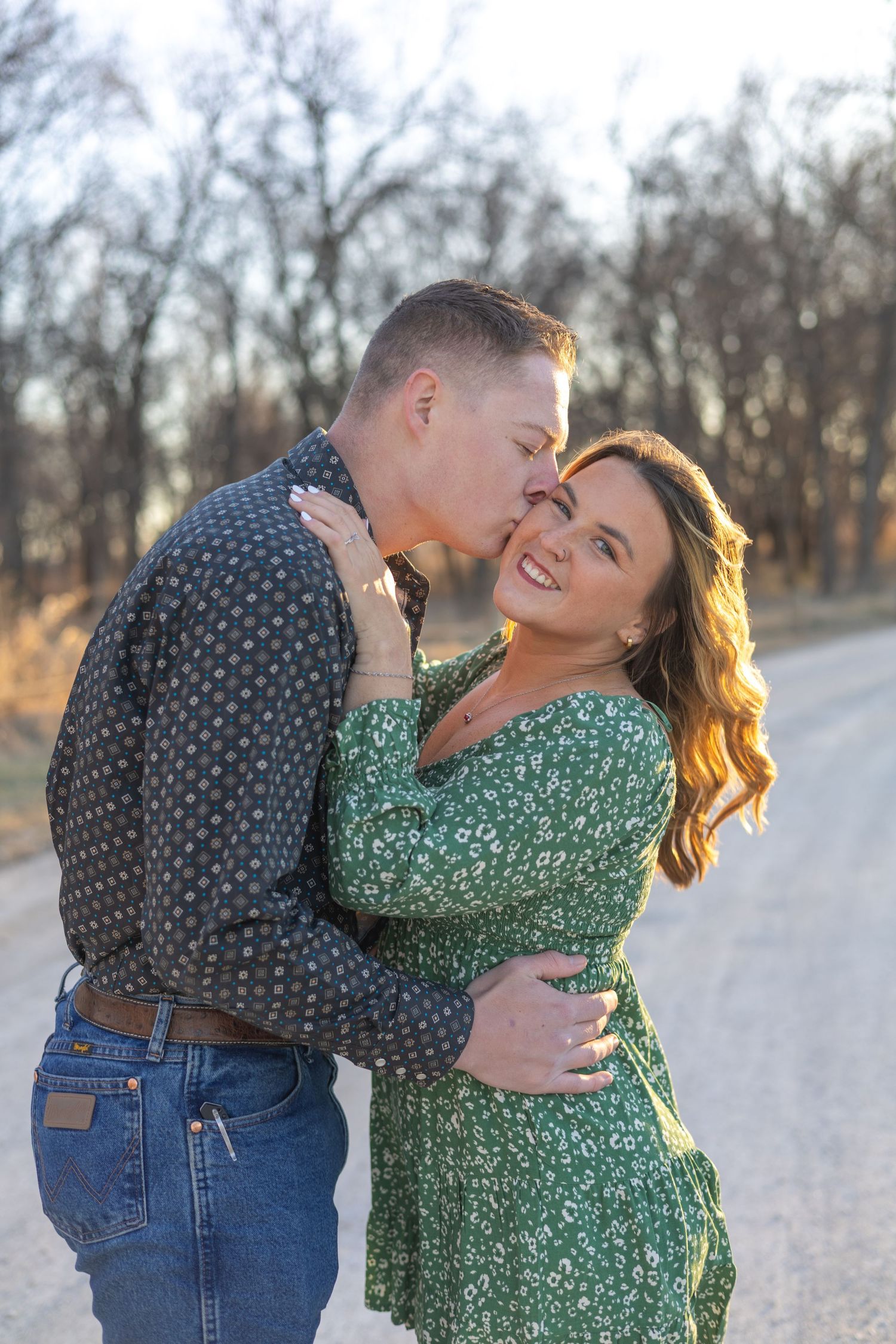 A couple in casual attire shares a tender moment on a gravel path during golden hour.