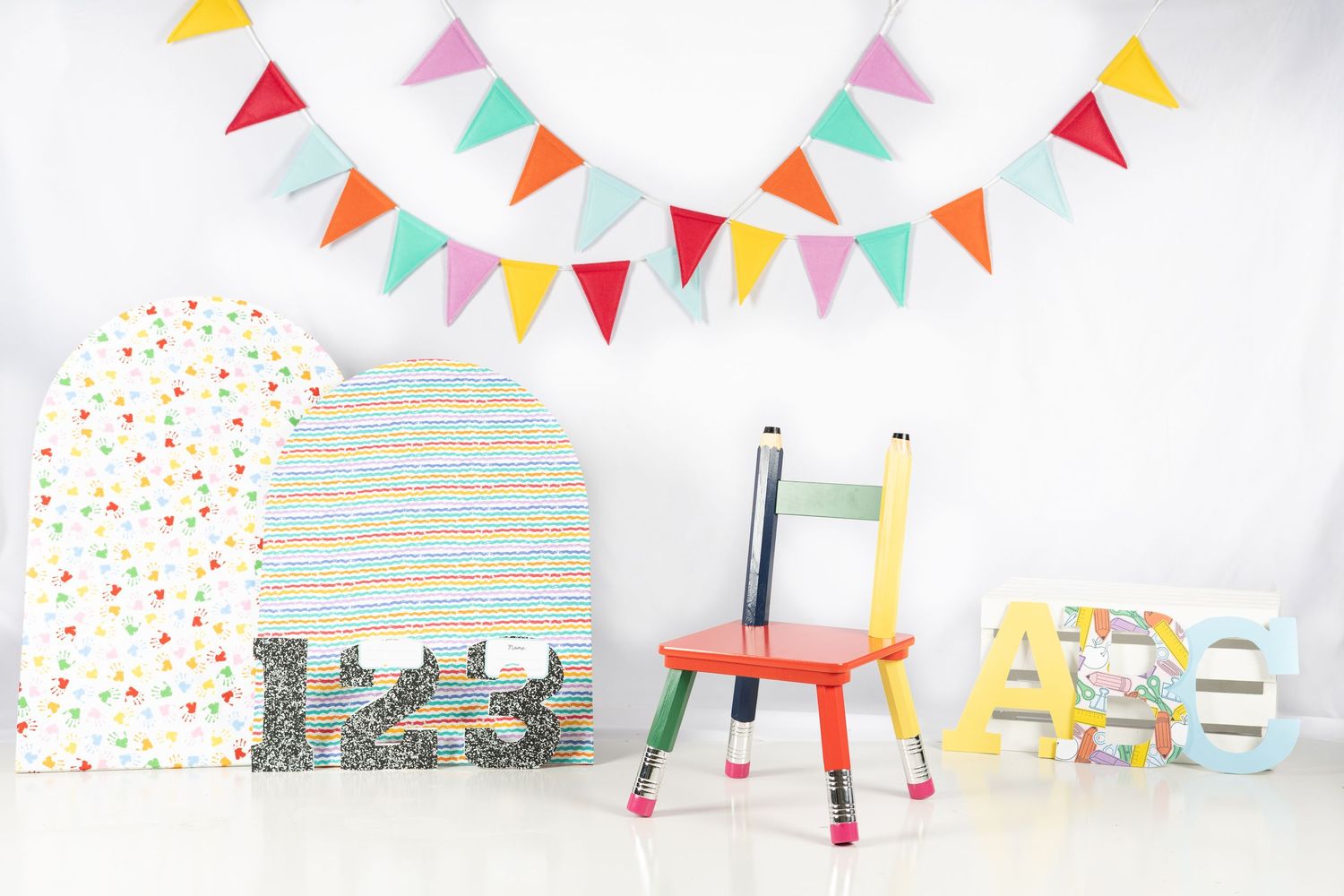 Colorful kids room decor with bunting flags, pencil chair, alphabet letters, and polka dot panels on white background.