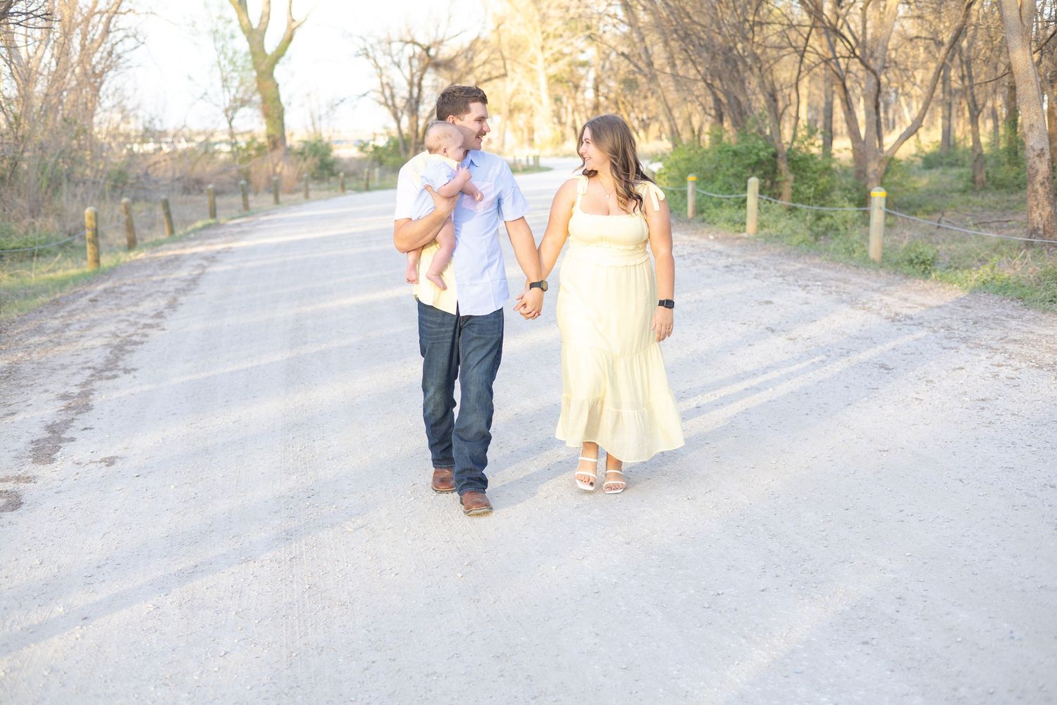 A couple walks hand in hand along a tree-lined path during a romantic outdoor photo session at sunset.