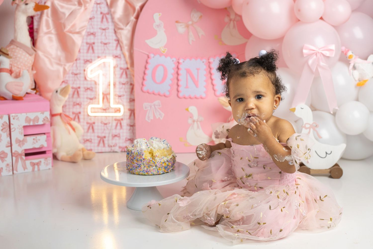 A baby girl in a pink dress smashes her first birthday cake at a pink-themed party.