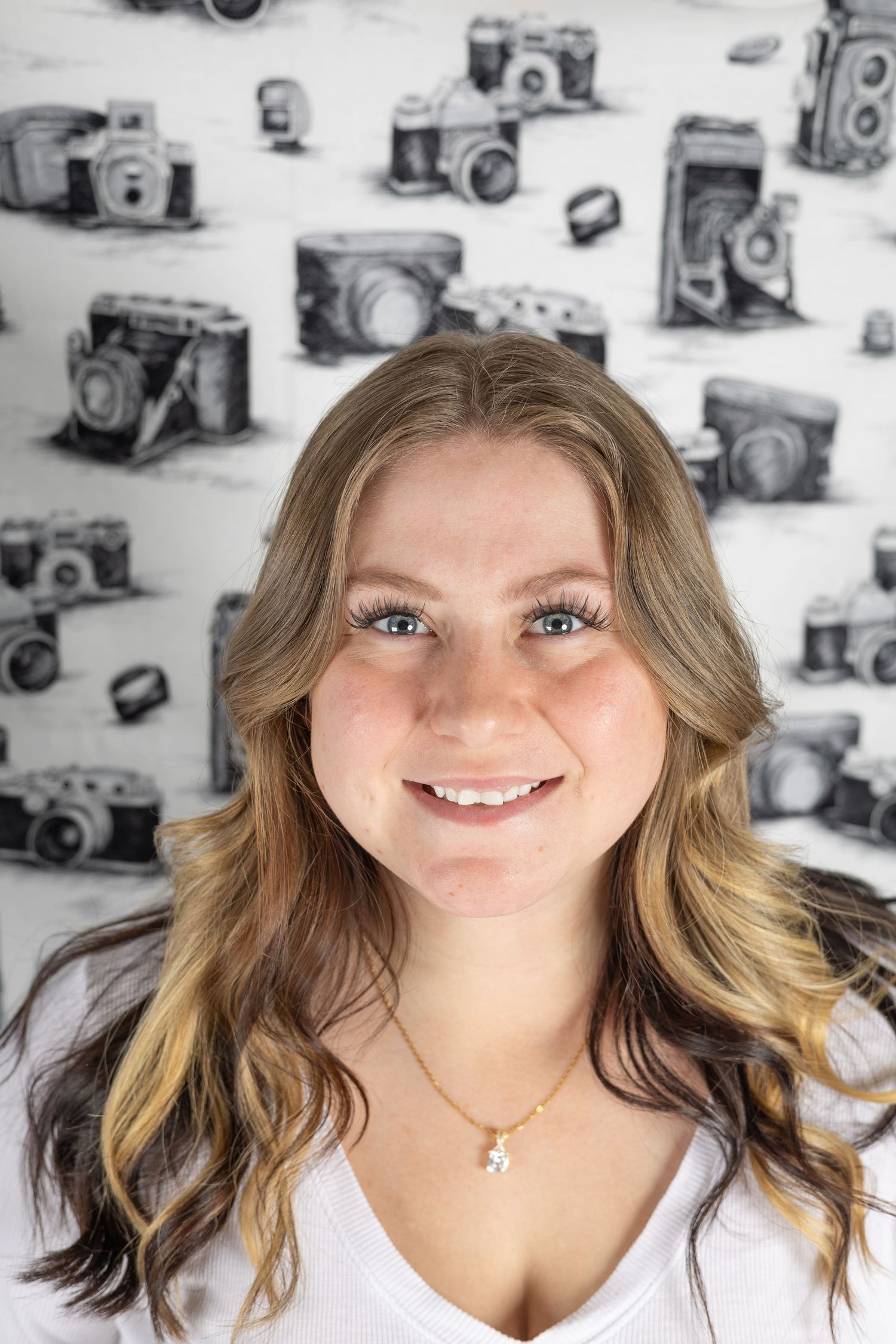 Four headshots of a person with wavy blonde hair against a background with vintage cameras.