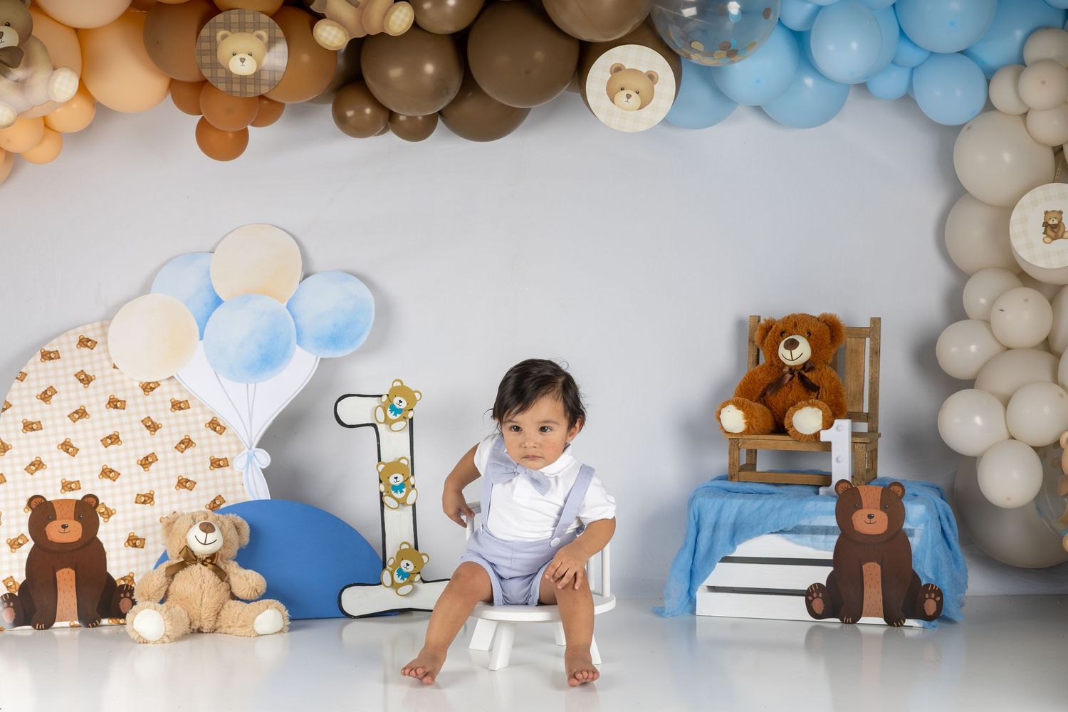 Baby boy sits among teddy bears and balloons at a bear-themed first birthday cake smash photo session.
