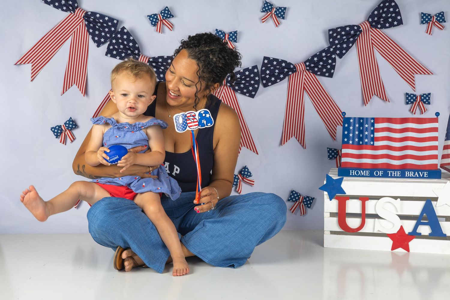 Woman and baby girl celebrate Fourth of July with patriotic decorations, American flags, and USA props in a festive photo.