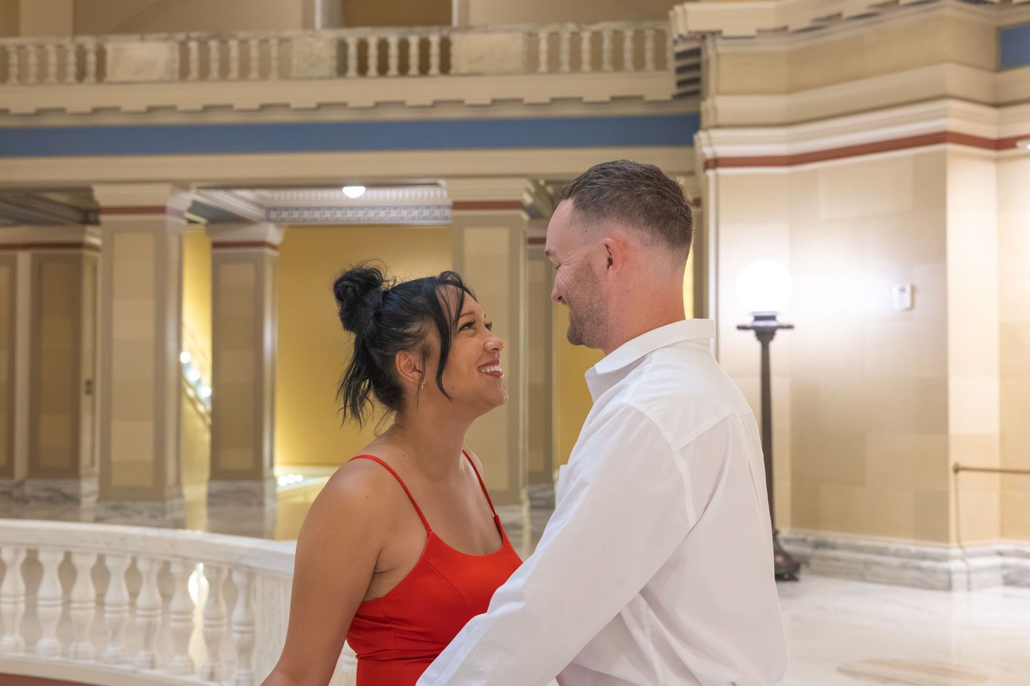 Couple in elegant hall, woman in red dress and man in white shirt sharing a romantic moment.