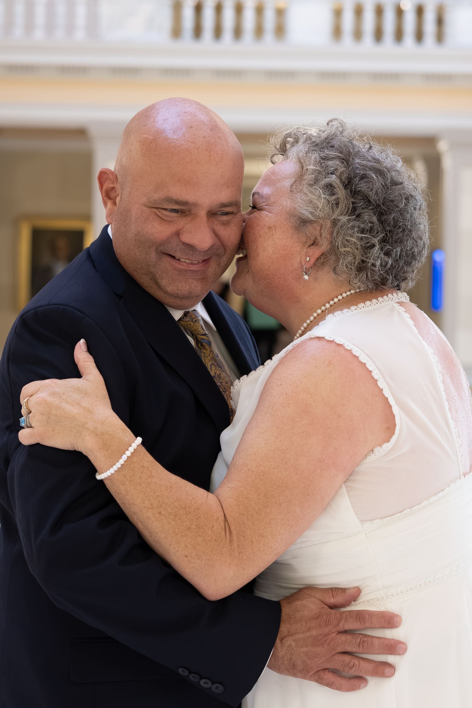 Elderly couple sharing a tender kiss during their wedding dance, bride in white dress and groom in navy suit.