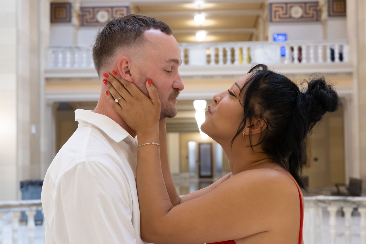 Romantic couple sharing an intimate moment in an elegant building, woman in red dress tenderly holding mans face.