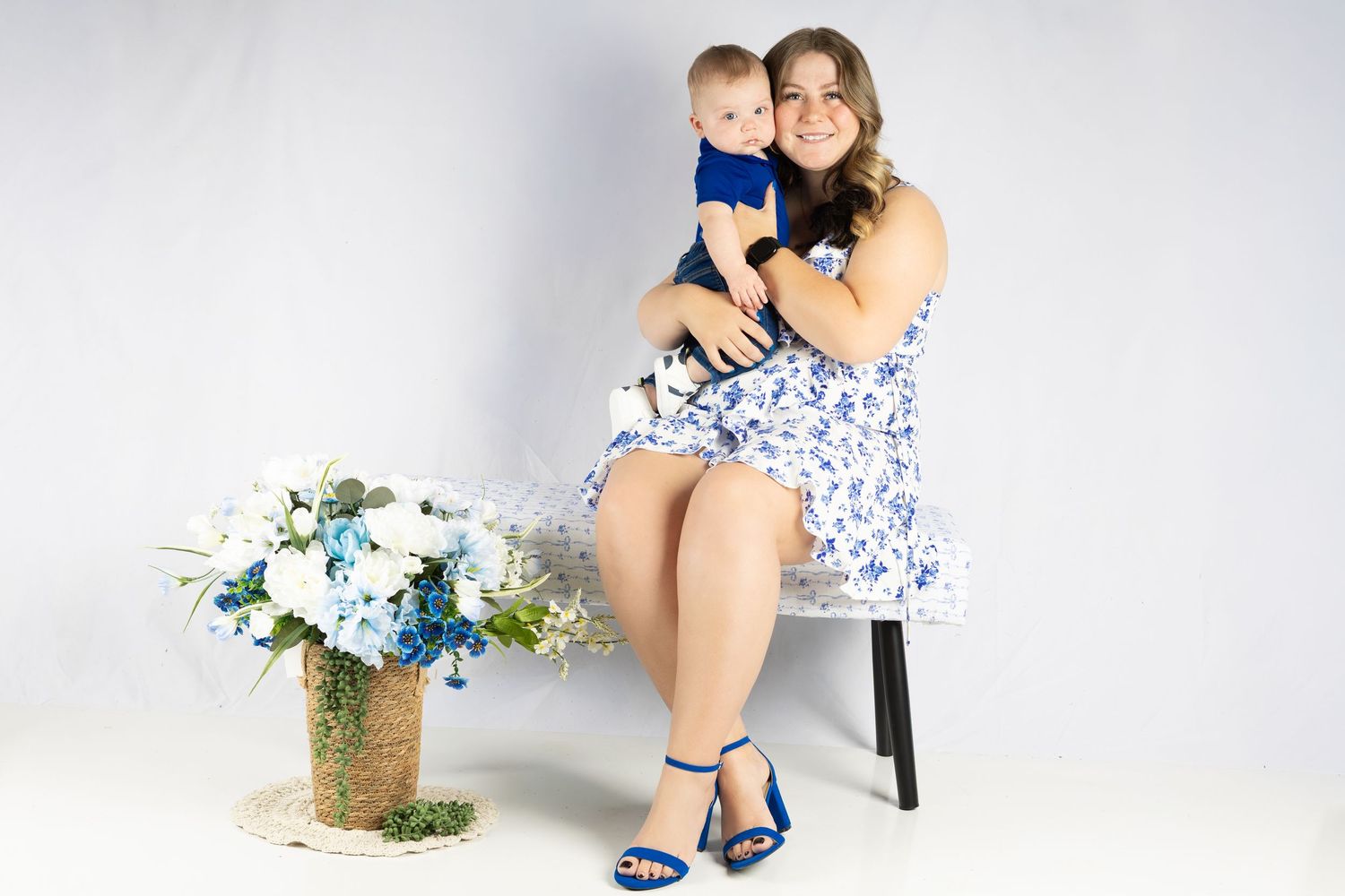 A floral arrangement sits beside someone in a blue and white patterned dress with matching blue heels on a stool.