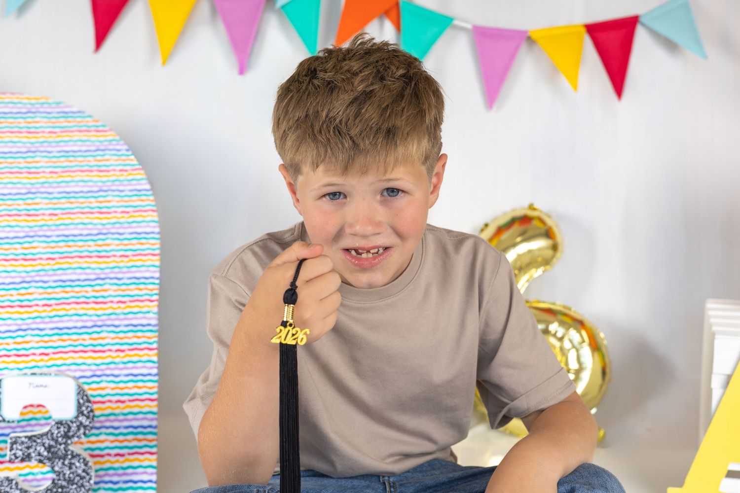 Happy boy with missing teeth smiles at birthday party, holding microphone with colorful bunting and gold number balloon.