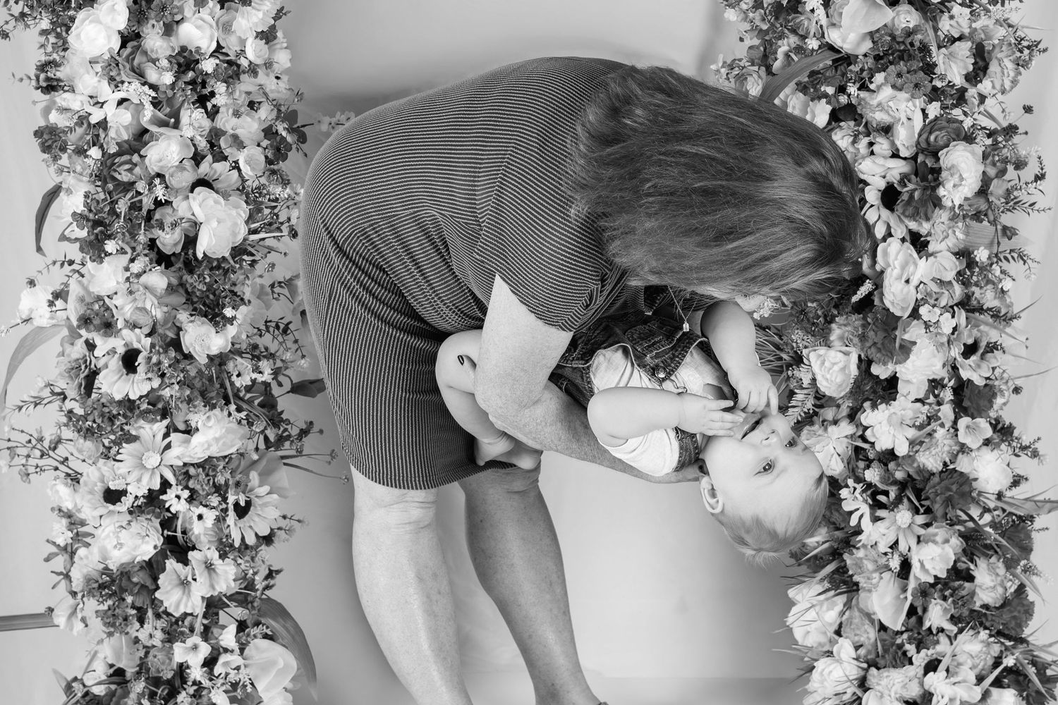 Black and white aerial photo of couple sharing romantic kiss surrounded by elegant floral arrangements.