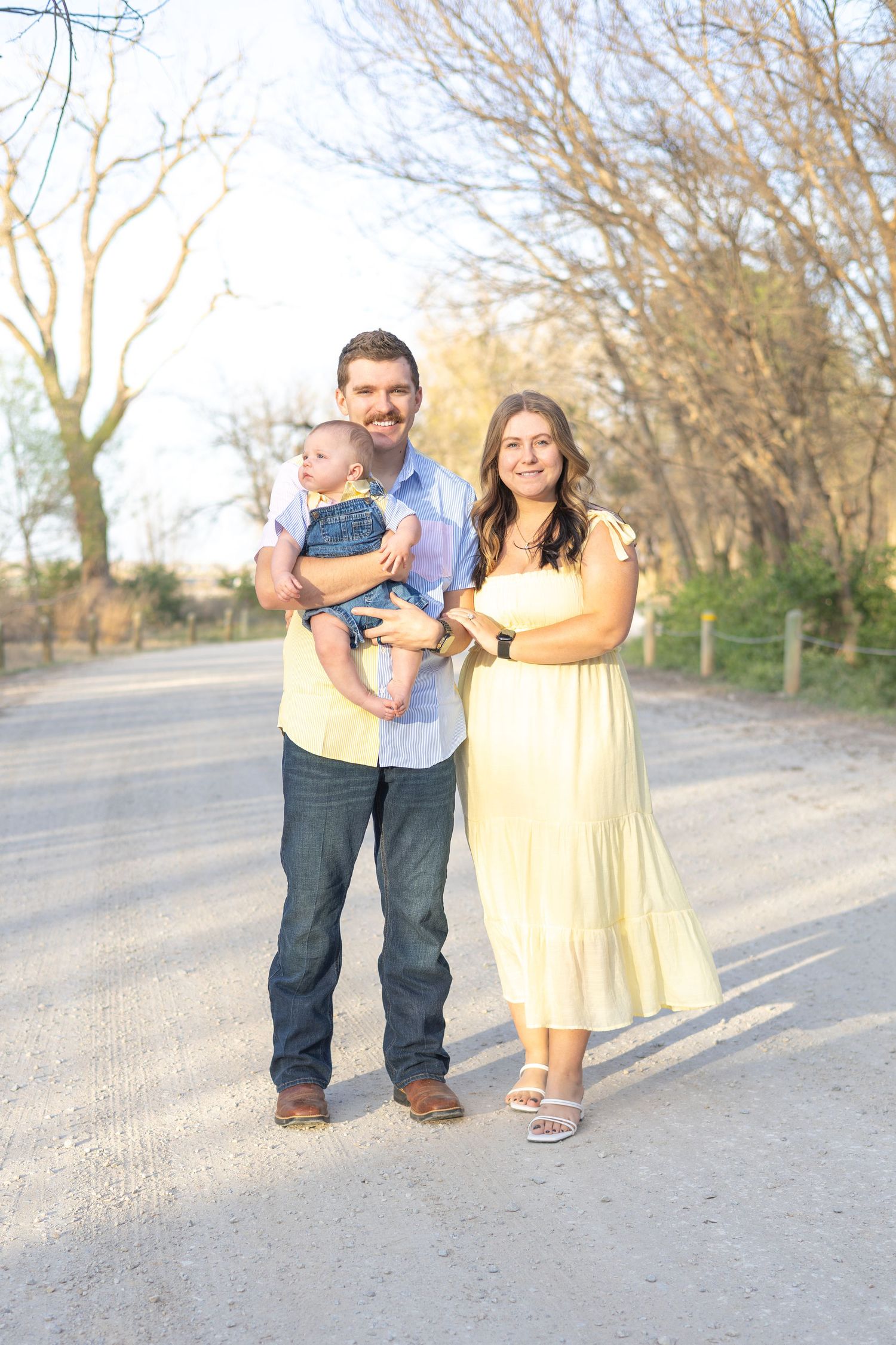 A family stands together on a dirt road during golden hour with trees in the background.