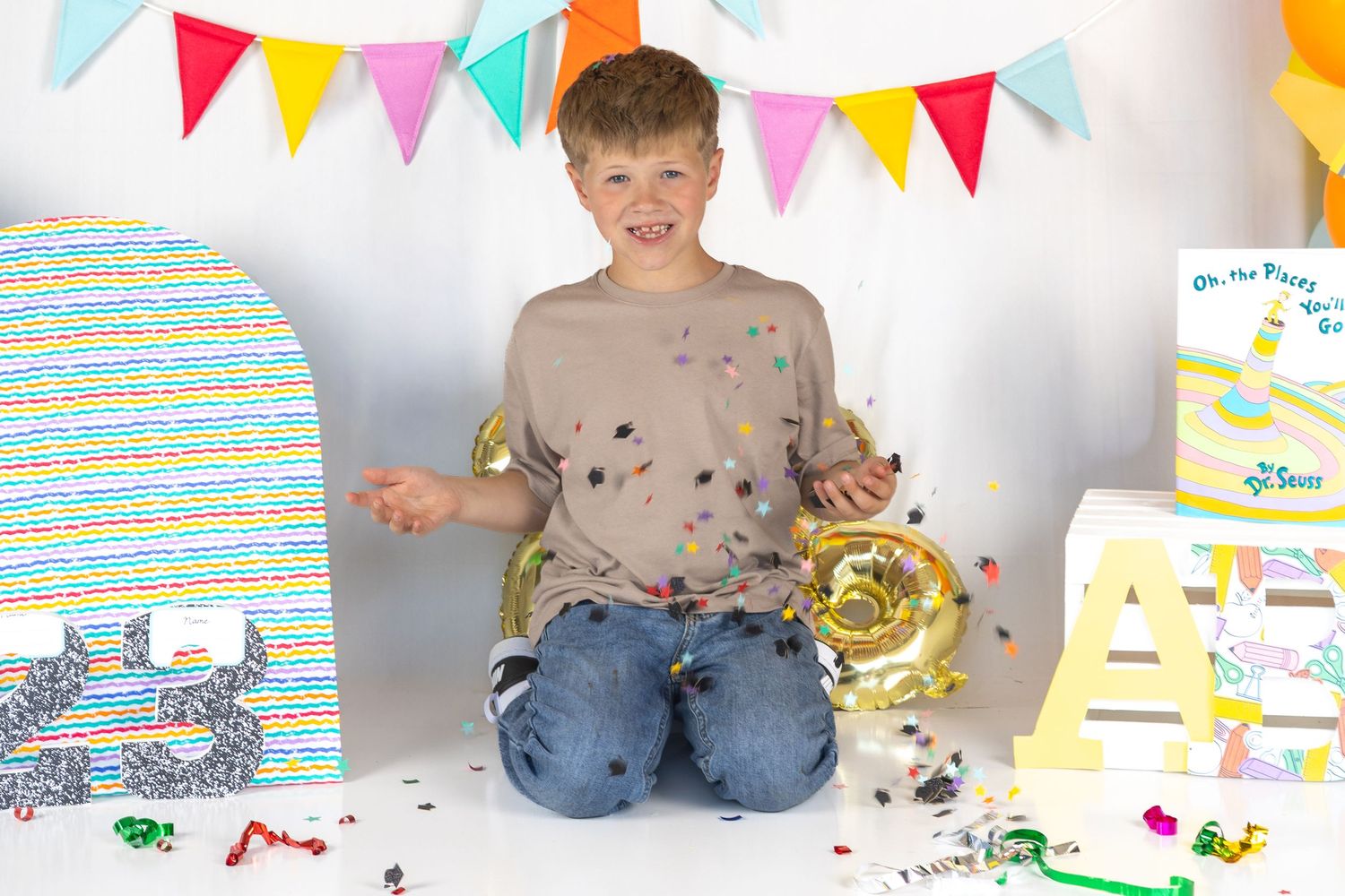 Happy boy sitting on floor covered in confetti with birthday balloons and party decorations around him.
