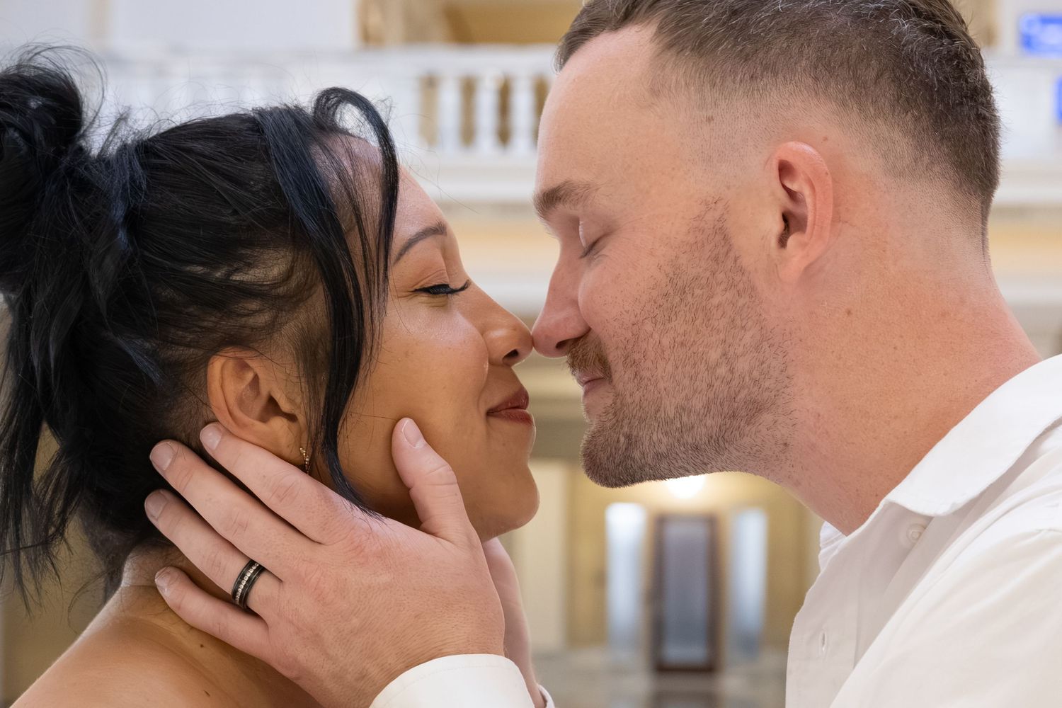 A couple shares an intimate moment, nearly kissing, as the groom tenderly holds the brides face during their wedding.