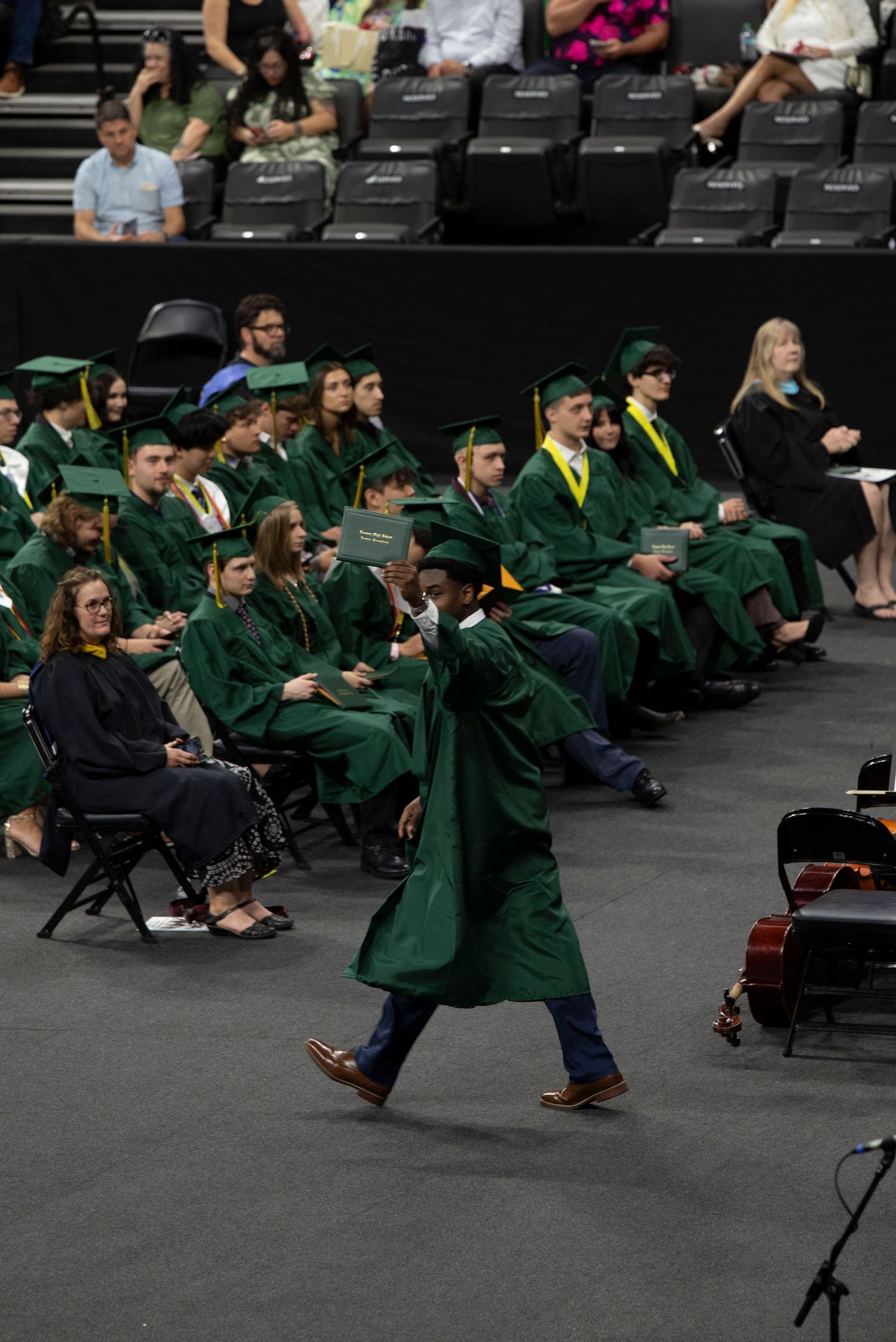 Graduate in green cap and gown walks across stage during commencement ceremony.
