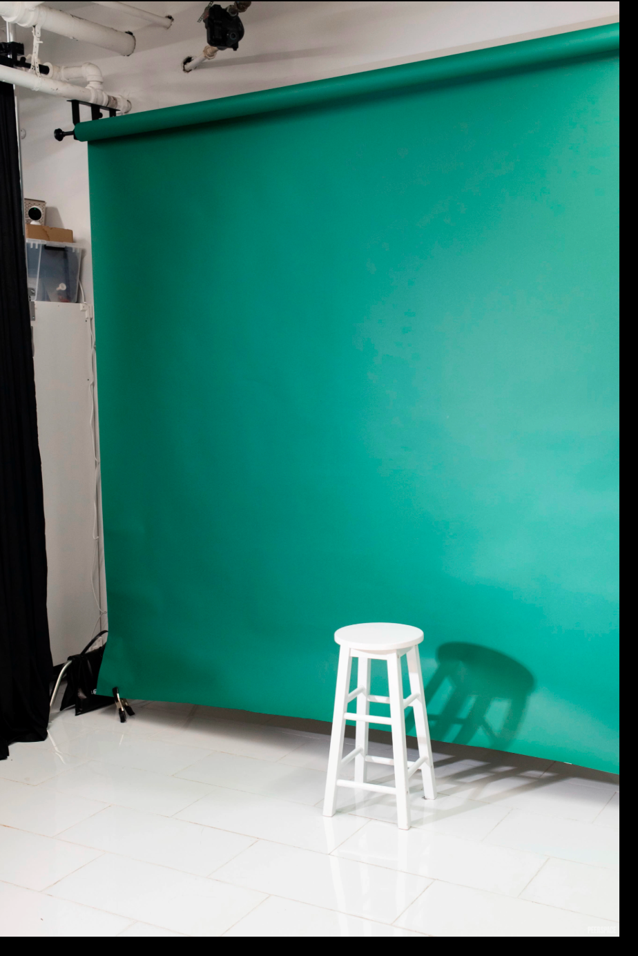 White stool in front of a teal green screen backdrop in a professional photography studio.