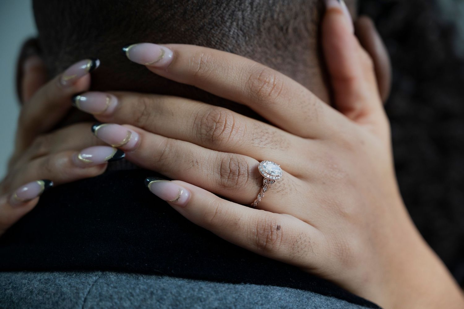 Close-up of hands with an engagement ring against a dark background.
