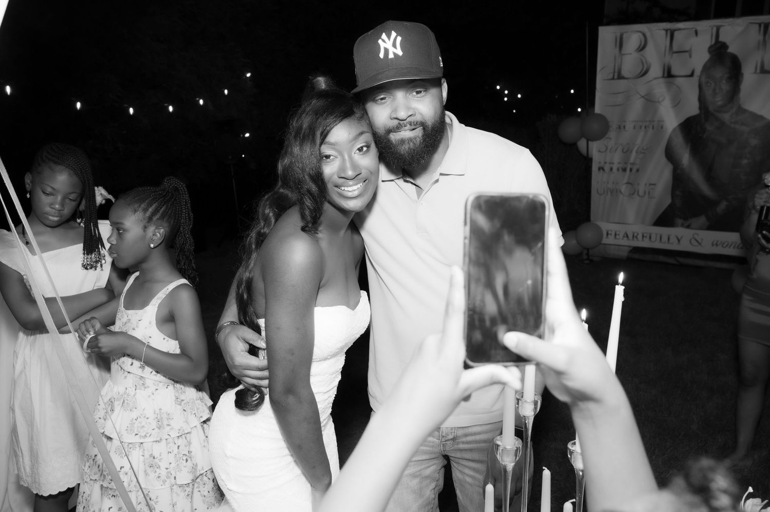 Black and white photo of two people posing for a selfie at an outdoor event with a BET sign in background.