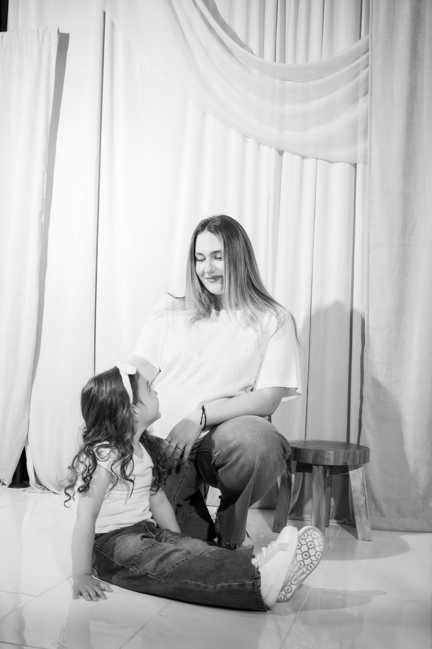 Artistic black and white boudoir photography with white flowing curtains in the background. Mother and daughter.