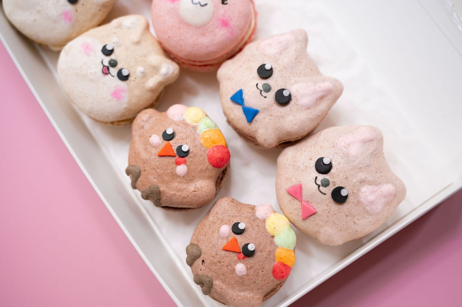 Cute decorated pink cookies with kawaii faces arranged on white serving plate.