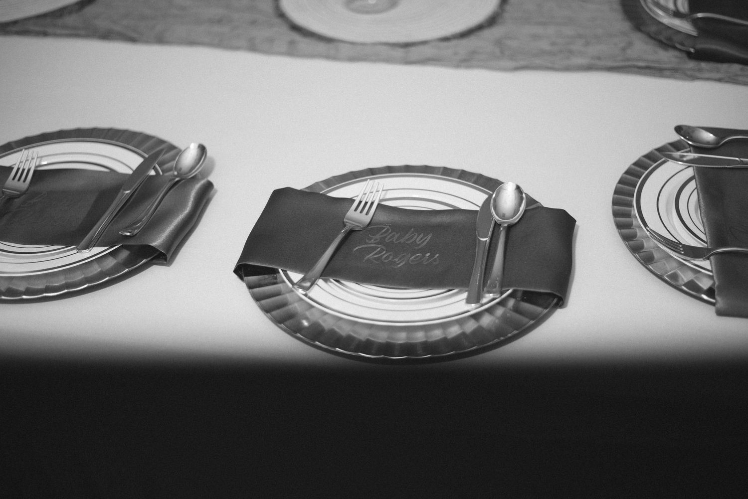 Black and white photo of elegant table setting with plates, silverware, and folded napkin with calligraphy place card.