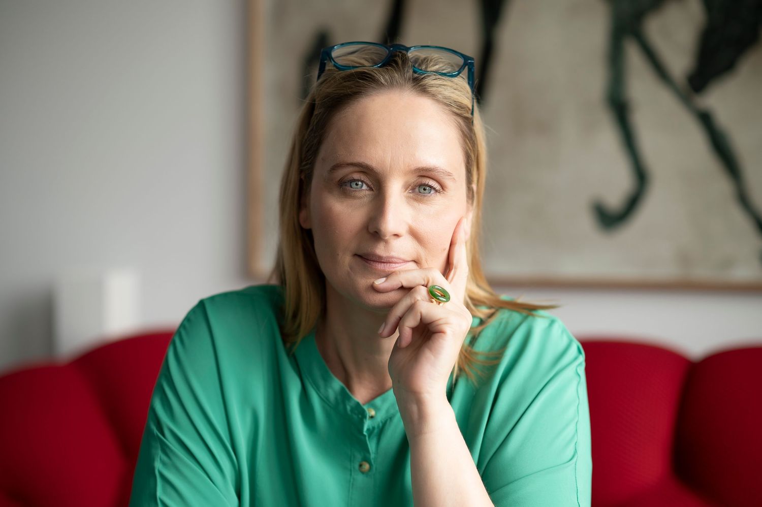 Woman in green blouse poses thoughtfully against red couch in professional portrait series.