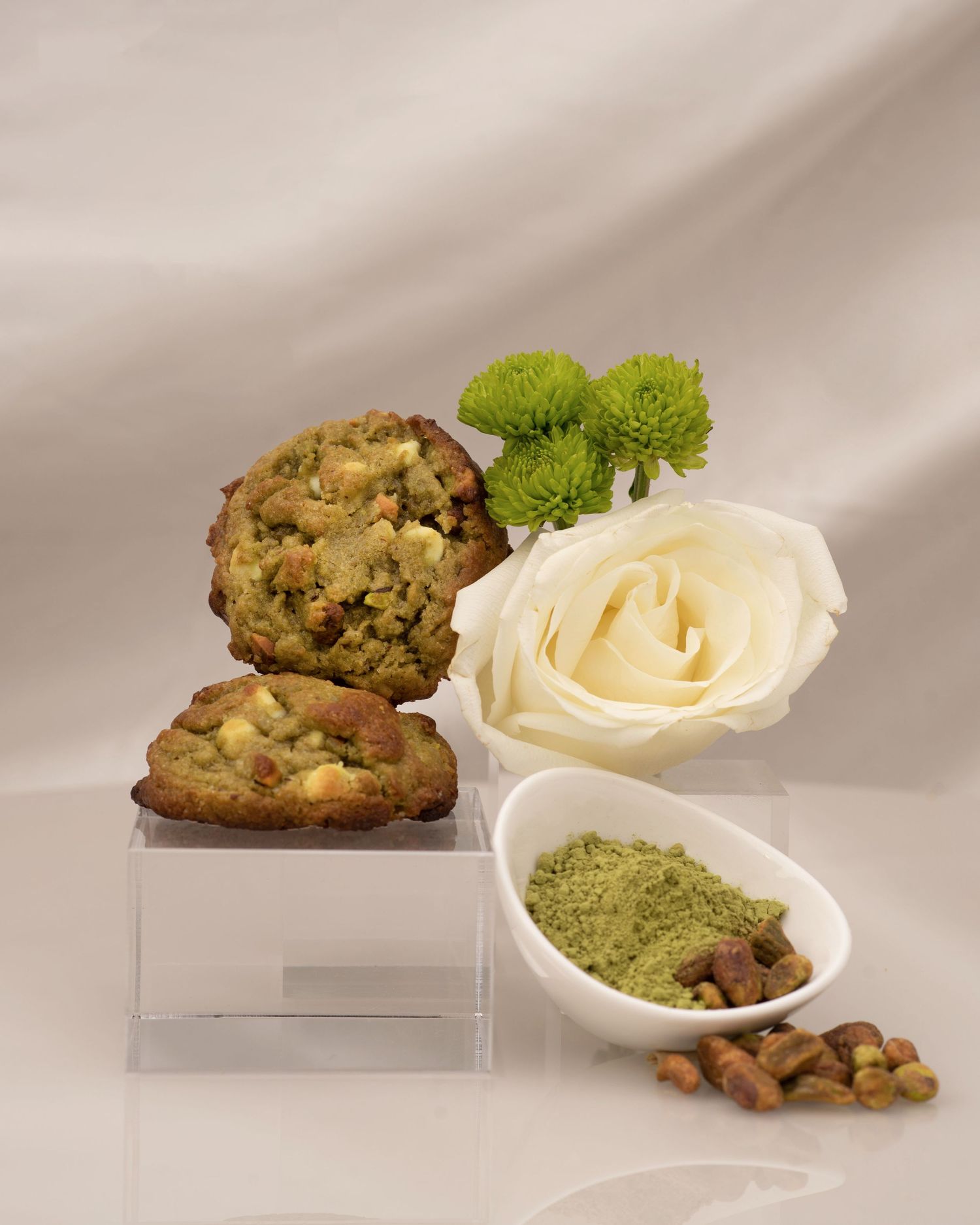 Styled product shot featuring white rose, green powder and baked goods on clear display stands.