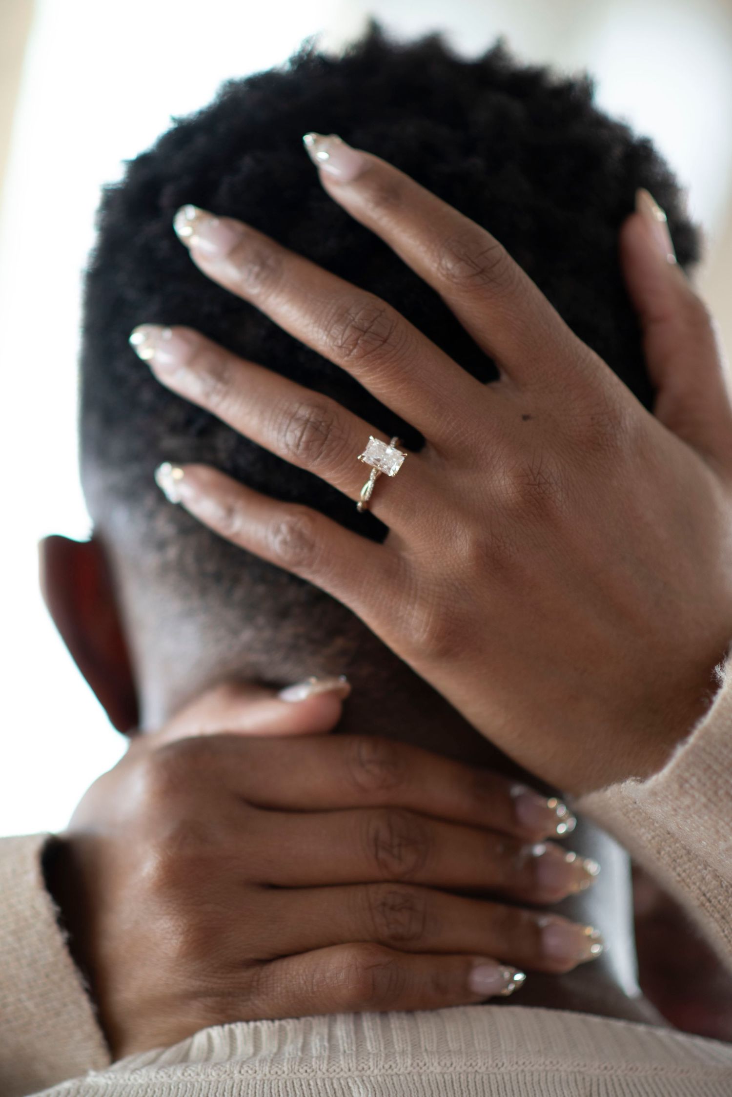 Close up of hands wearing engagement rings against a light background.