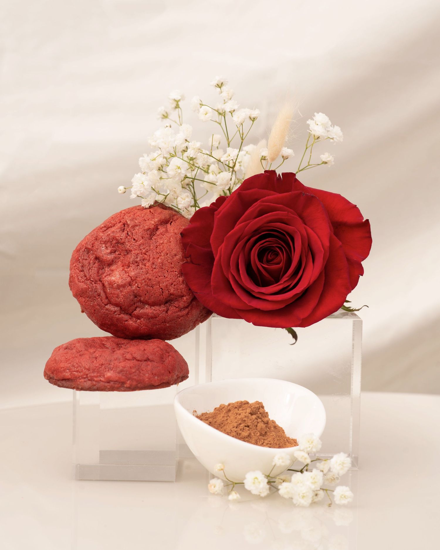 Product photography of red rose and powder ingredients on white display pedestals.