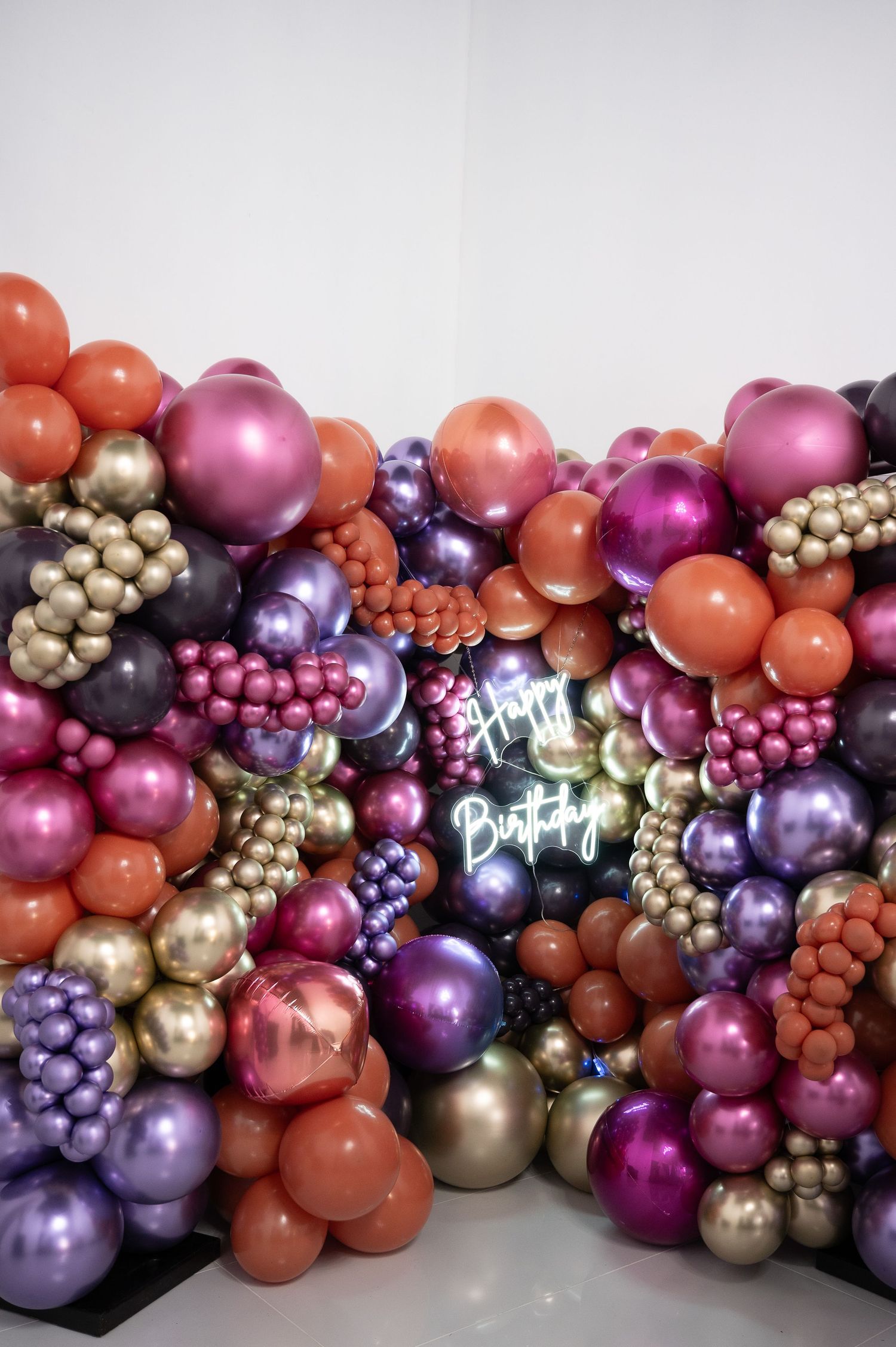 Vibrant birthday balloon wall featuring chrome purple, gold, pink, and orange balloons with a neon Happy Birthday sign.