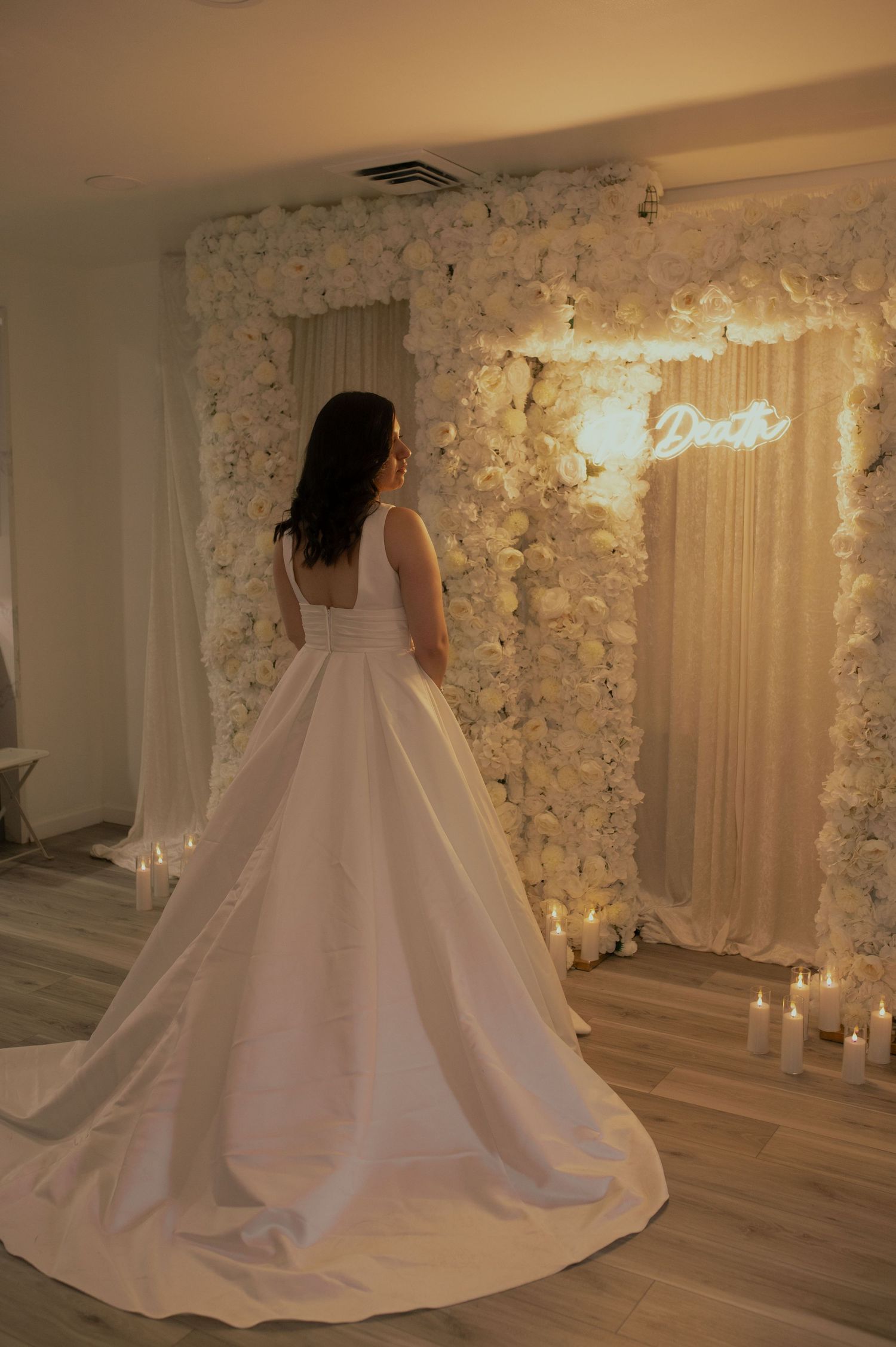 A flowing white wedding gown trails across a floor decorated with floral walls and candles.