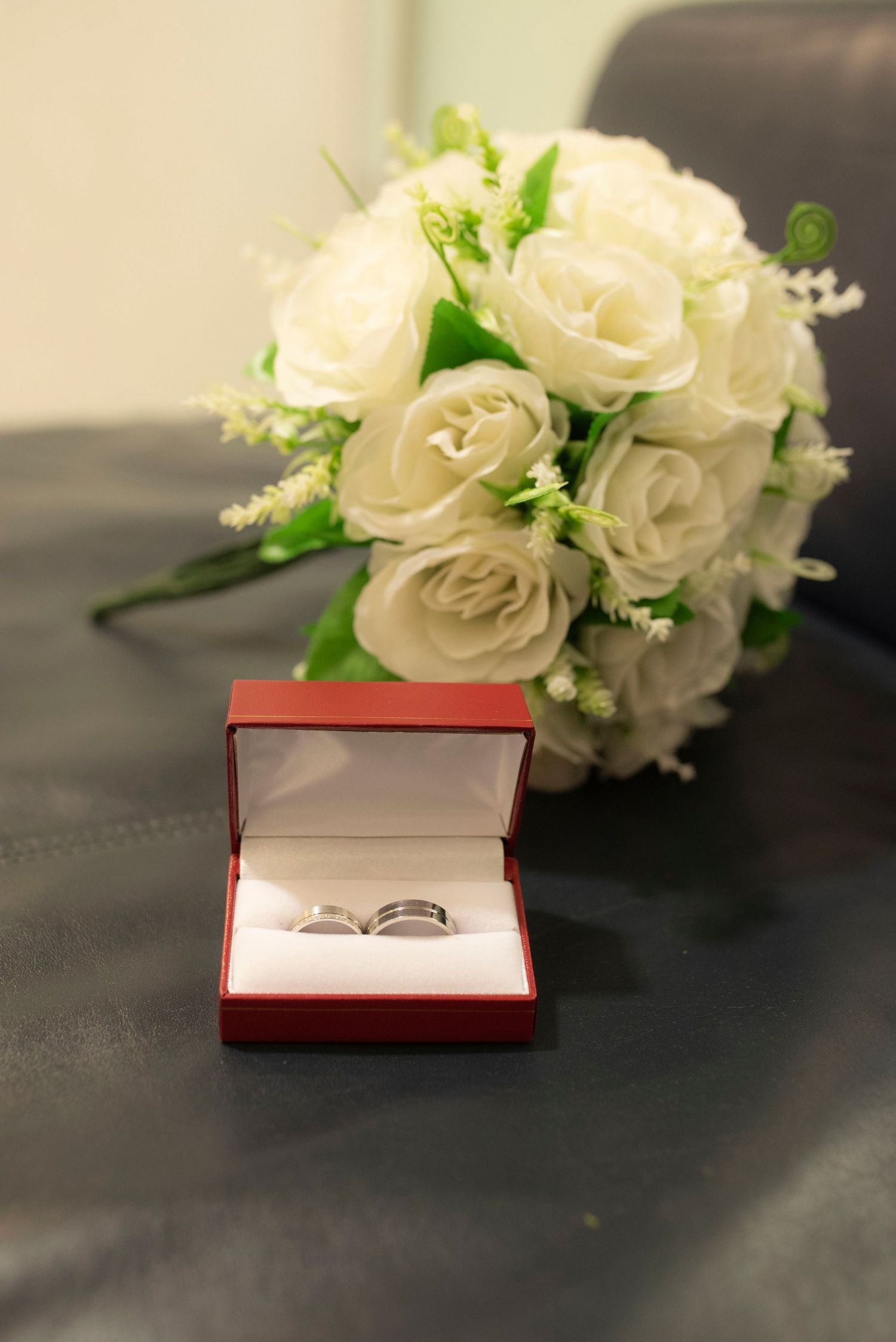 White roses and engagement ring box displayed on dark surface.