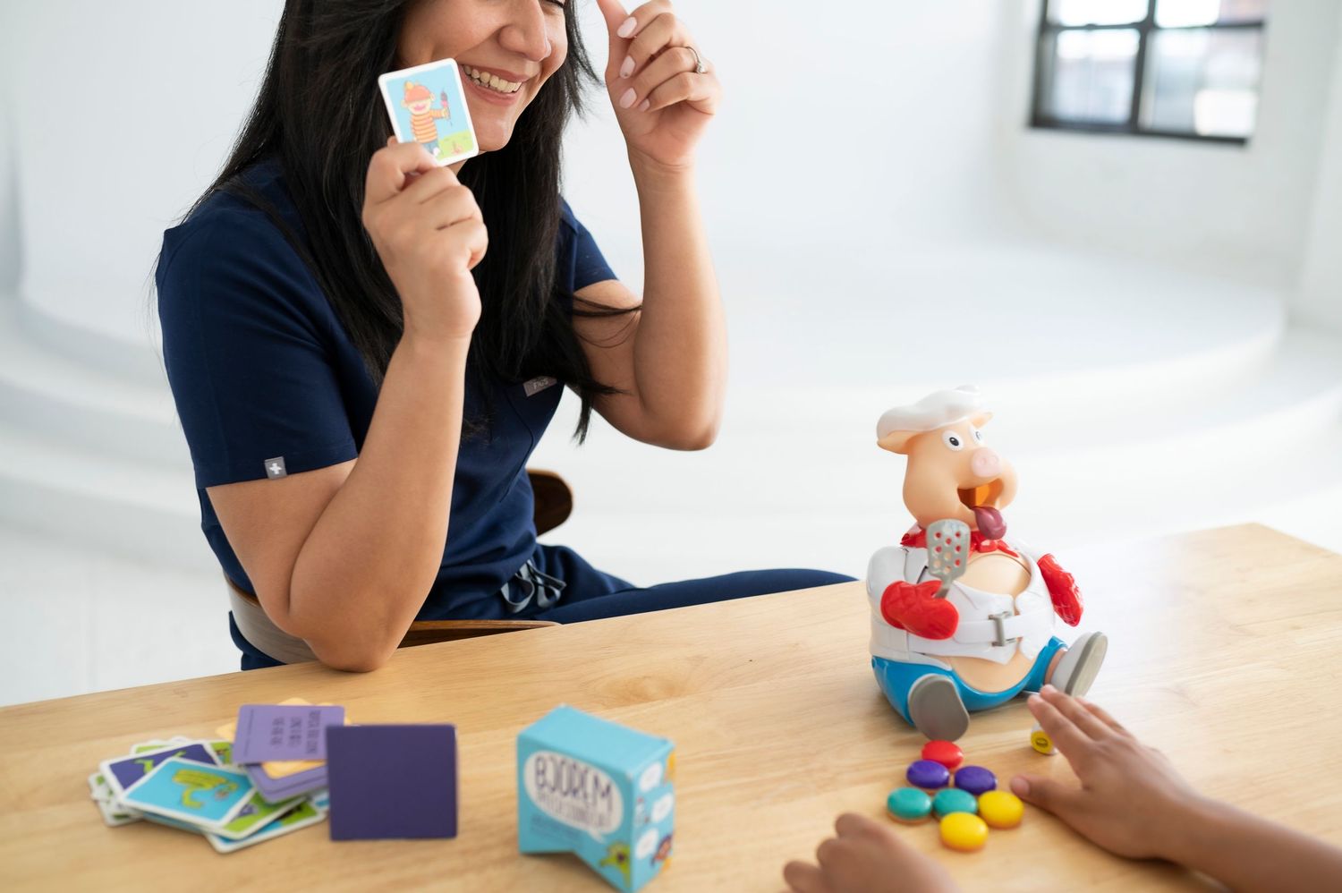 Playful scene of someone holding game cards with colorful toys on a table.