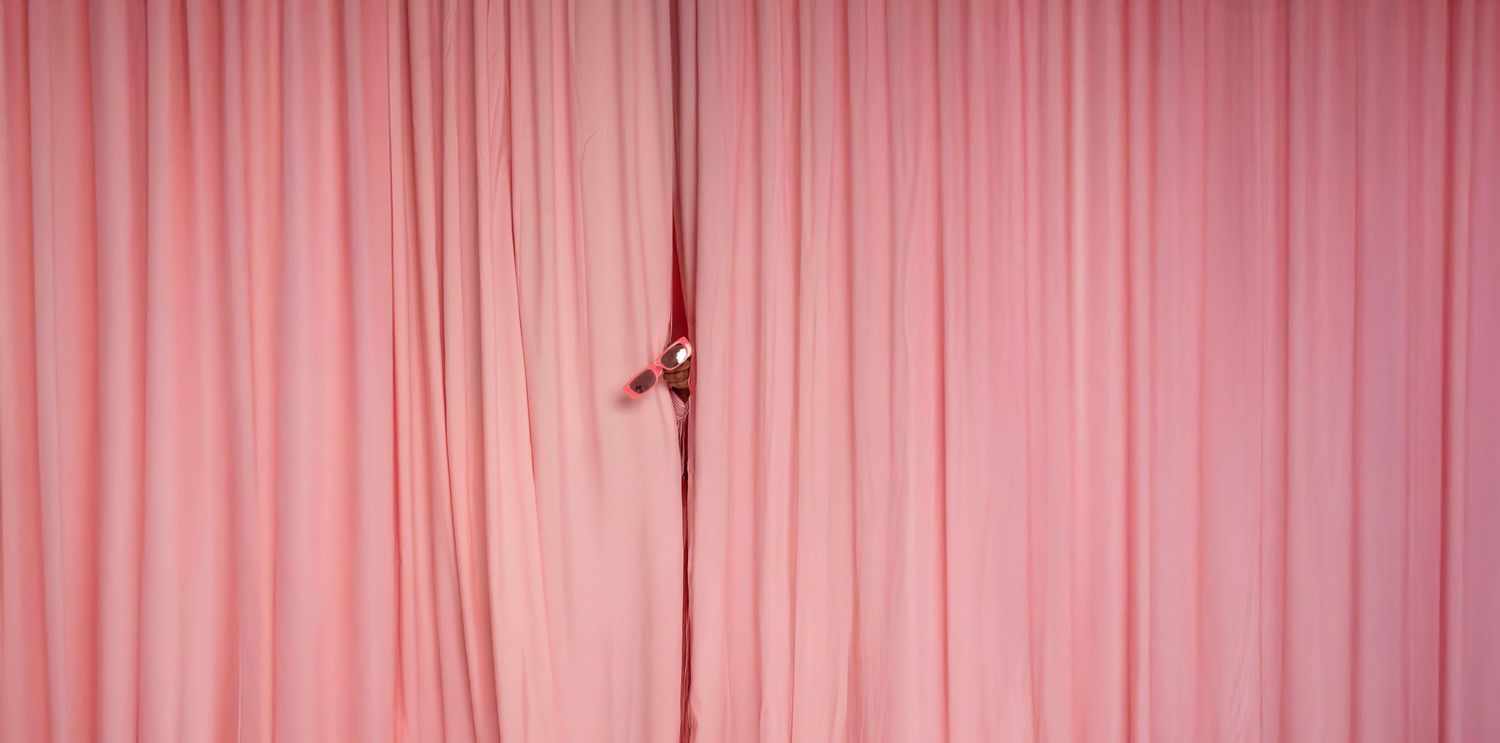 A pink curtain or drape hangs in vertical folds creating a soft textured background.