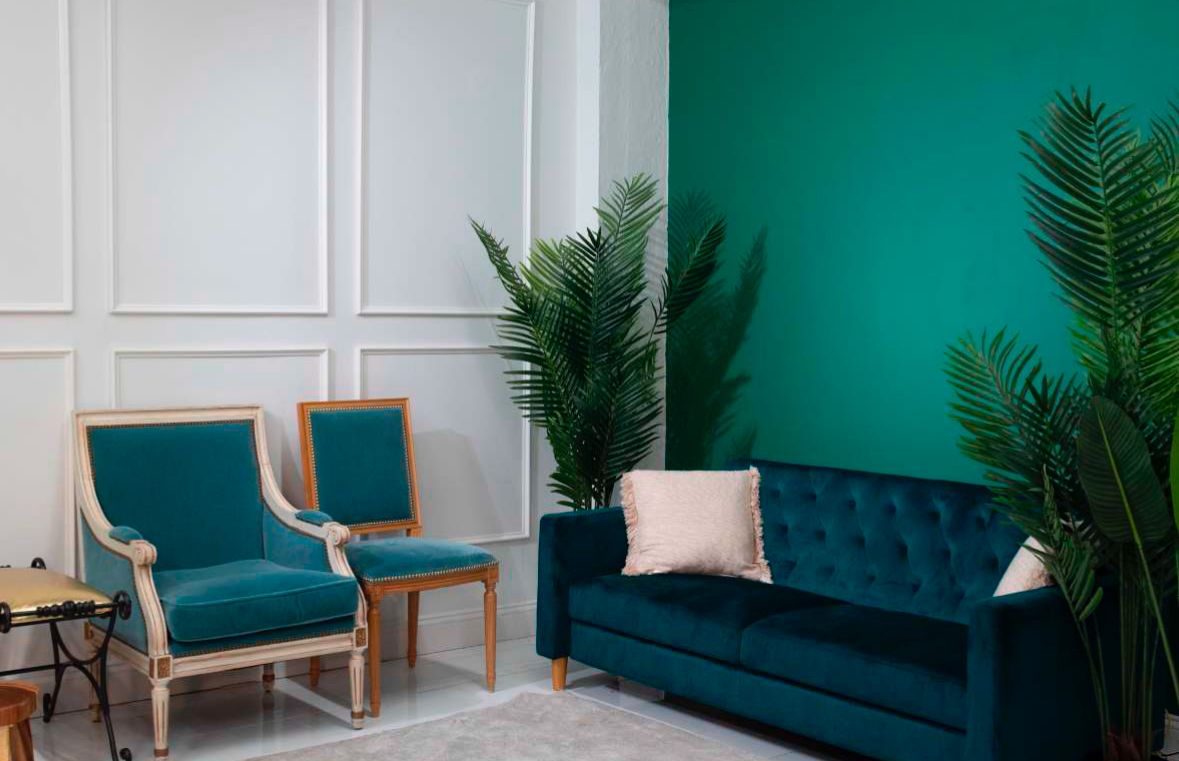 Elegant living room with teal velvet sofa, two vintage armchairs, and lush palm plants against a teal accent wall.