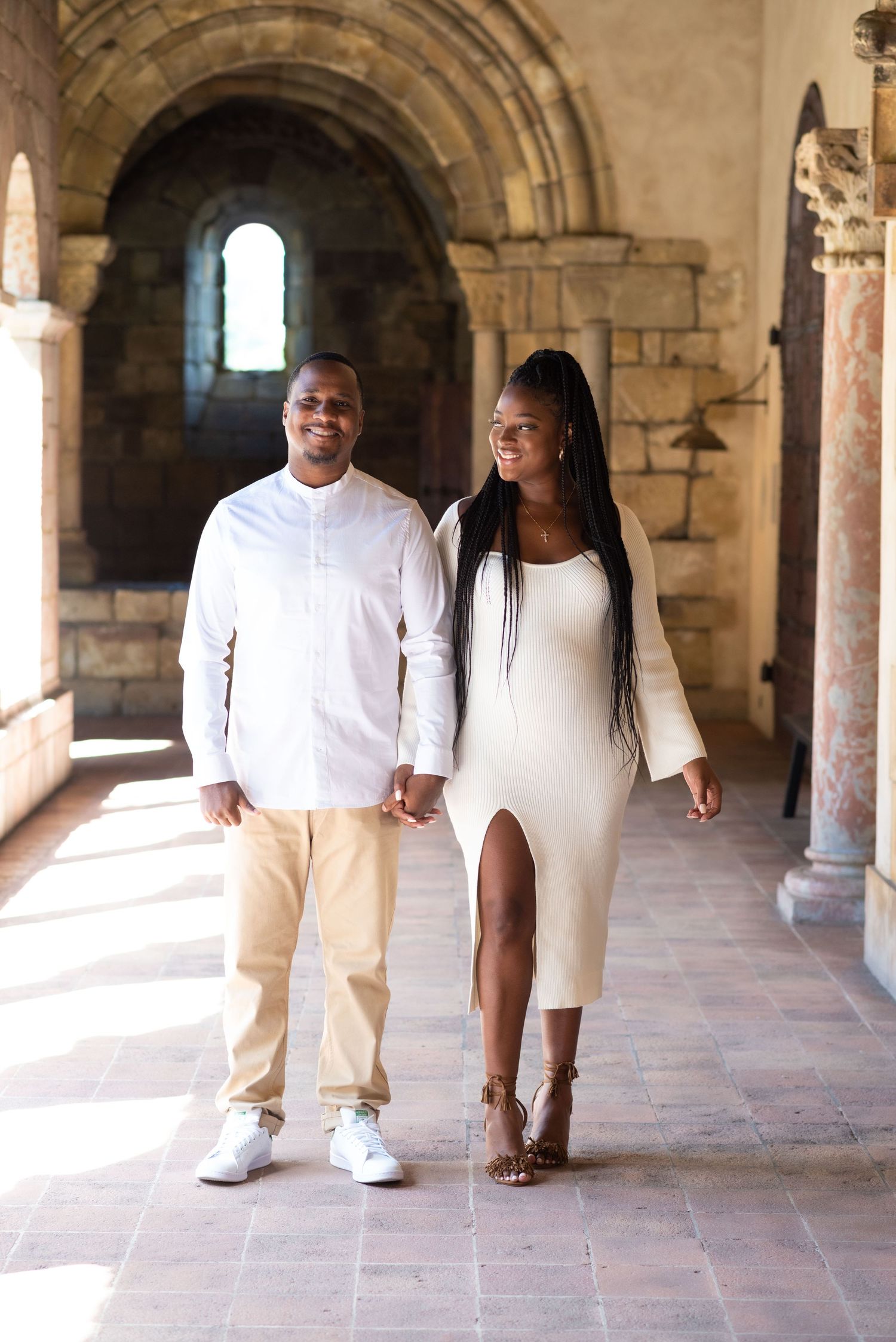 Couple walking through historic stone archways in coordinated white outfits.