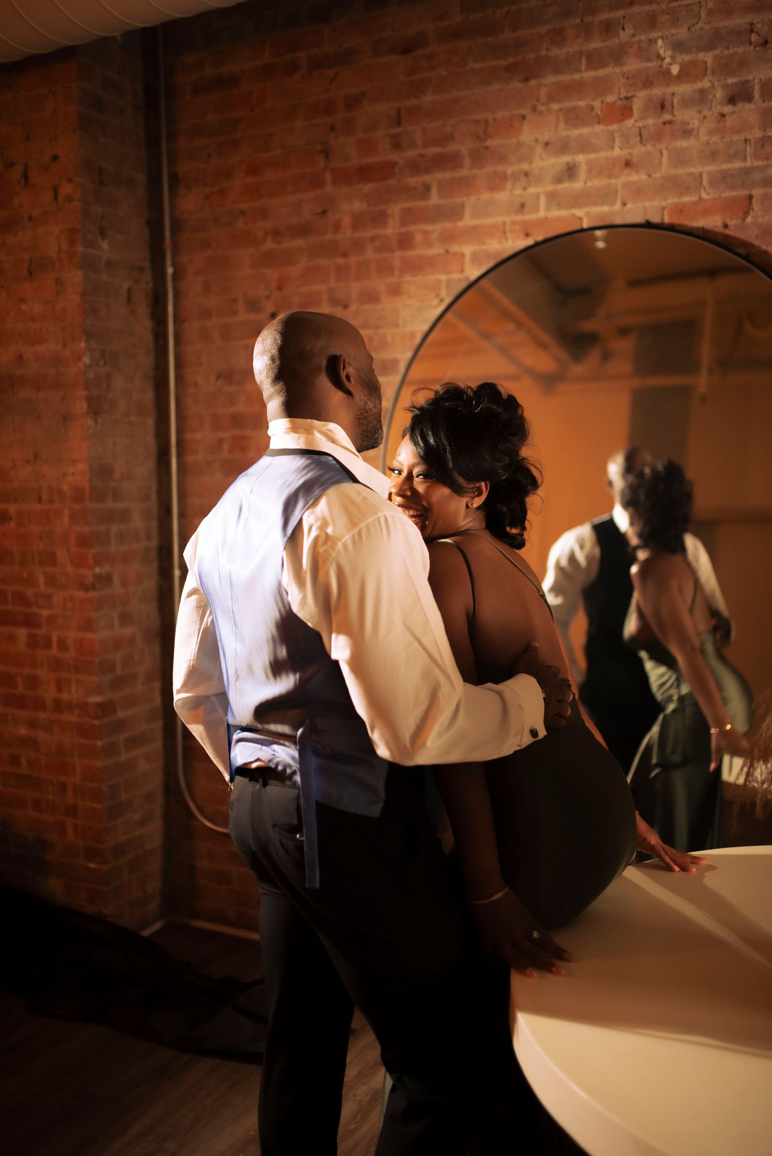 A couple shares an intimate dance moment against a rustic brick wall backdrop.