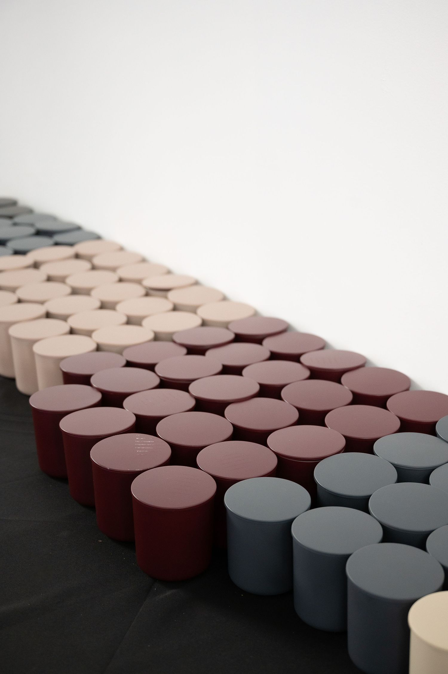 Rows of colorful cylindrical objects in beige, burgundy, and gray arranged in a geometric pattern on a dark surface.