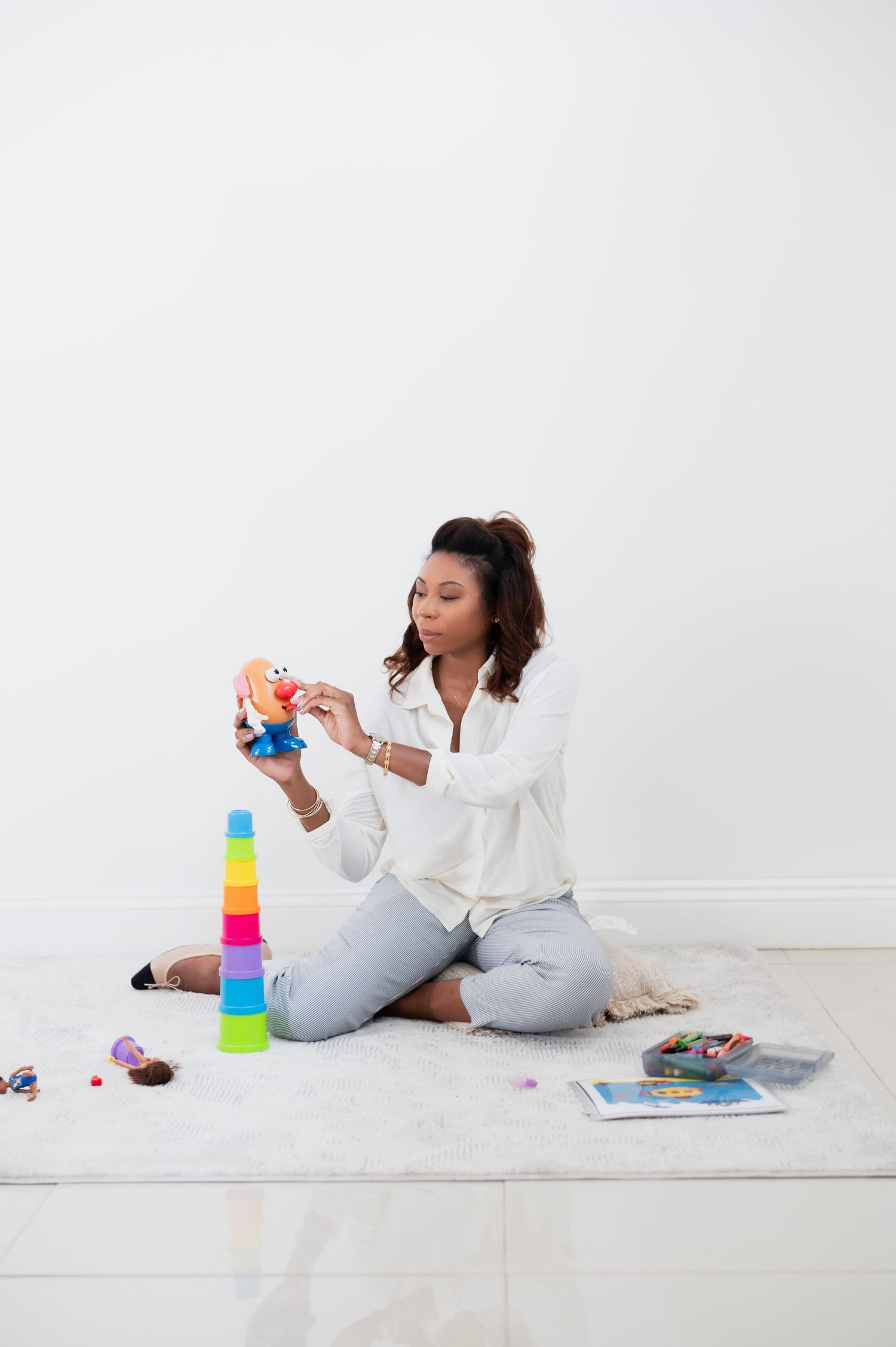 Person in white shirt and jeans playing with colorful stacking toys on white floor.