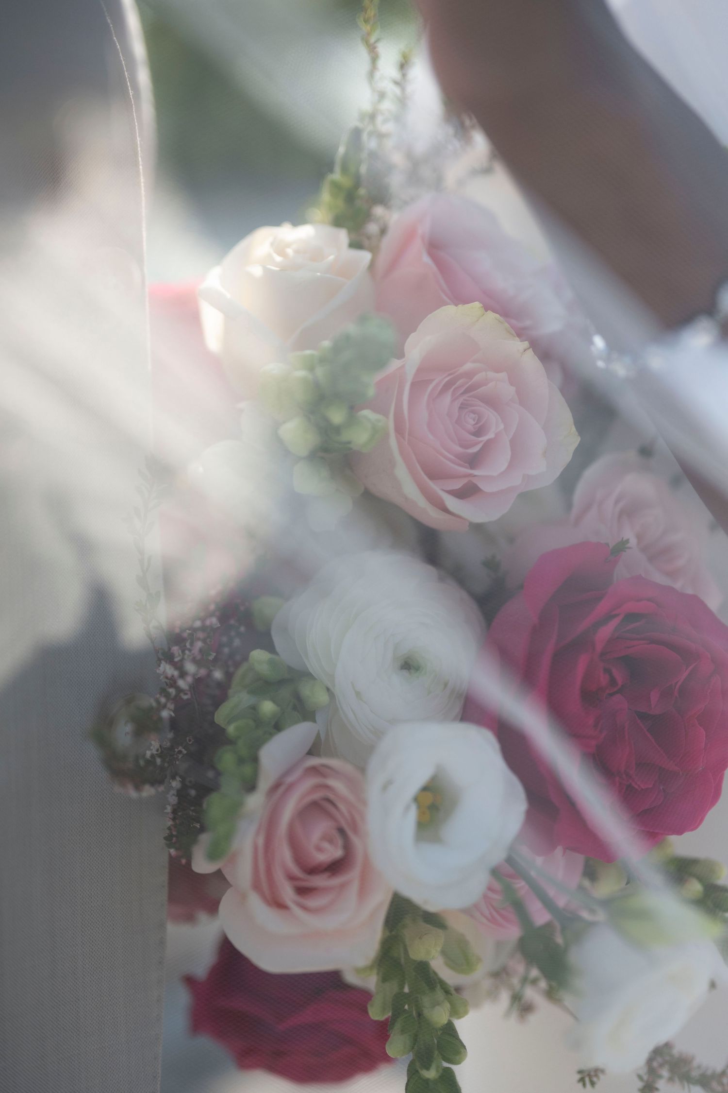Soft bridal bouquet featuring pink and red roses with white ranunculus in a dreamy, ethereal light.