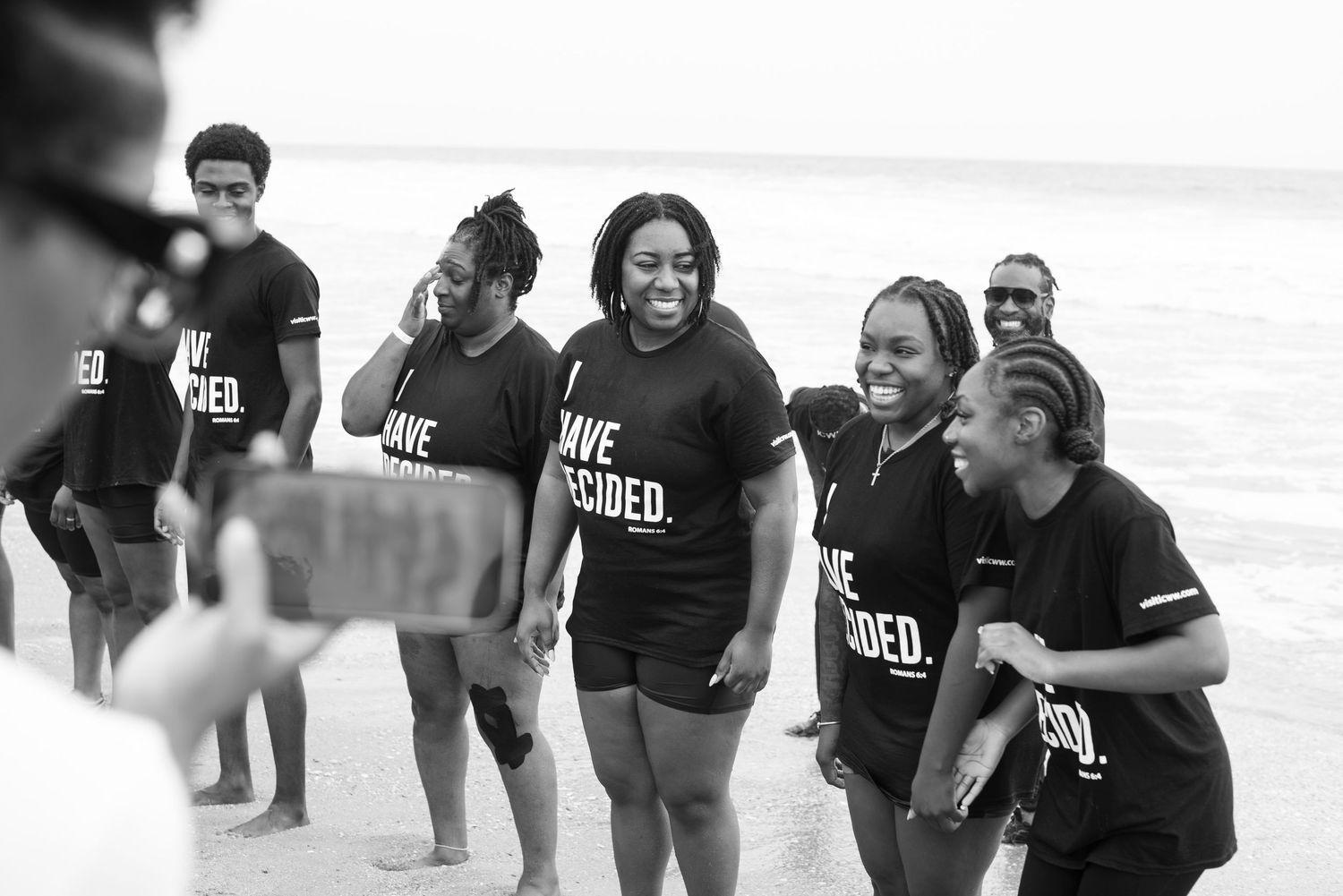 Group of young people wearing matching black 'I Have Decided' t-shirts posing for a photo on a beach.